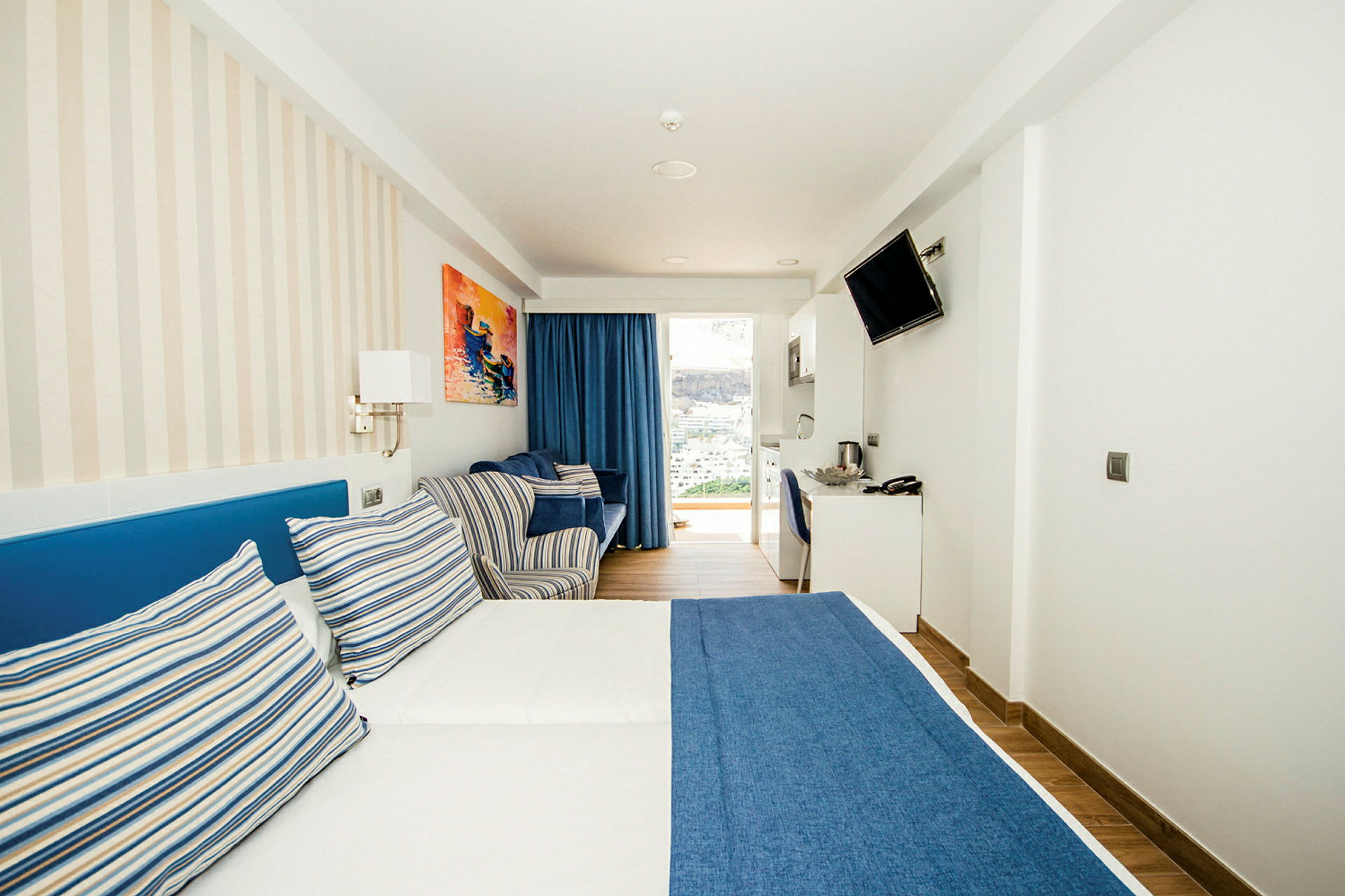 Hotellihuone, jossa on parisänky sinisellä päiväpeitteellä ja raidallisilla tyynyillä. (Tekoälyn luoma teksti)