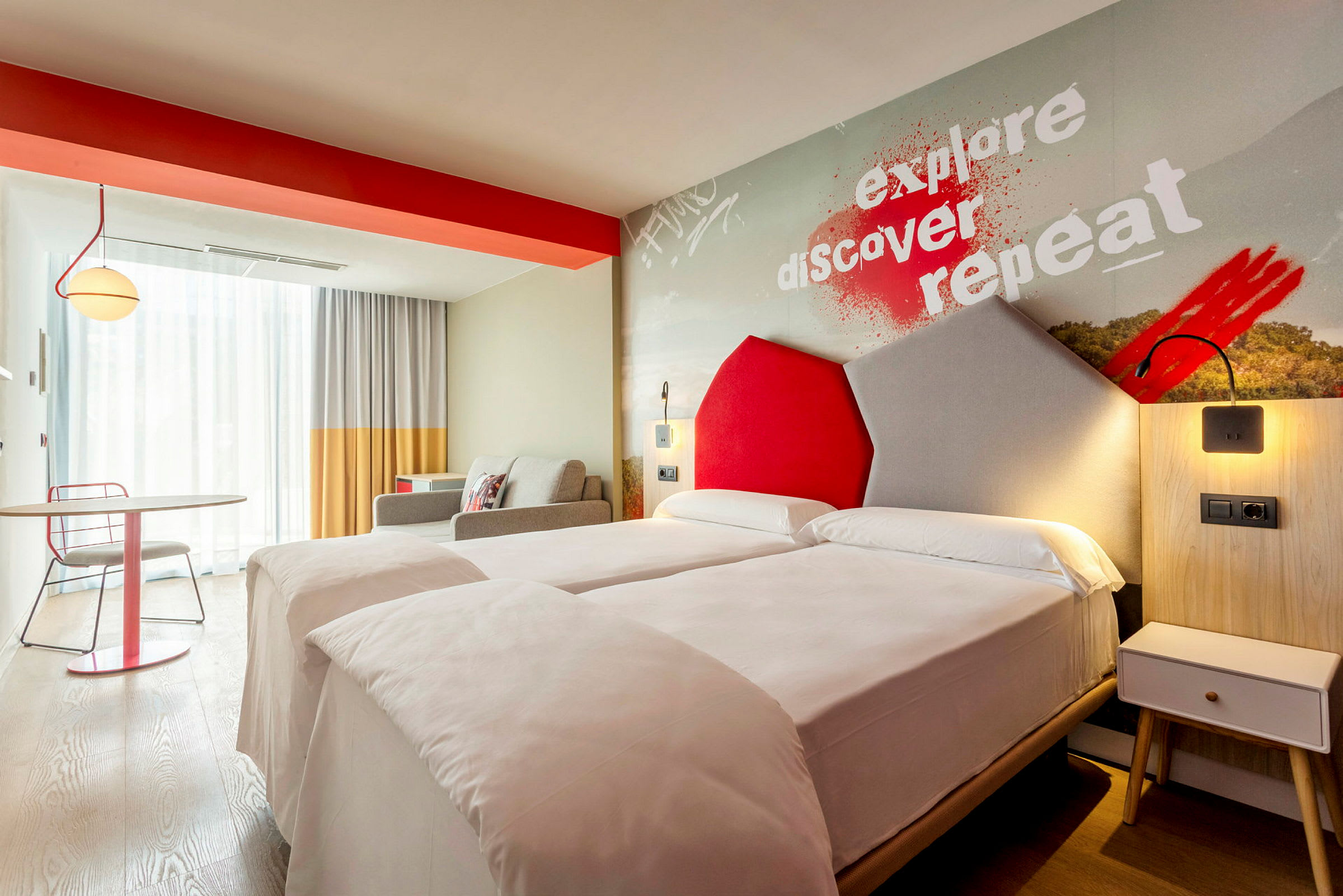 Moderni hotellihuone, jossa on kaksi yhden hengen vuodetta ja värikkäitä yksityiskohtia. (Tekoälyn luoma teksti)