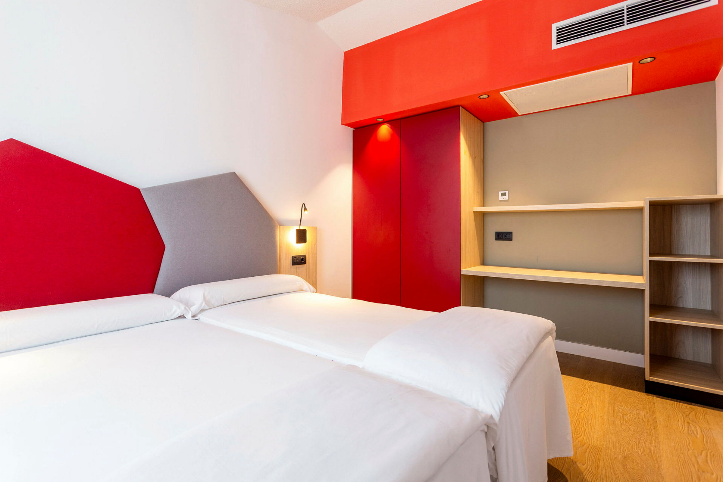 Hotellihuone, jossa on kaksi yhden hengen vuodetta, värikäs seinäsuunnittelu ja hylly. (Tekoälyn luoma teksti)