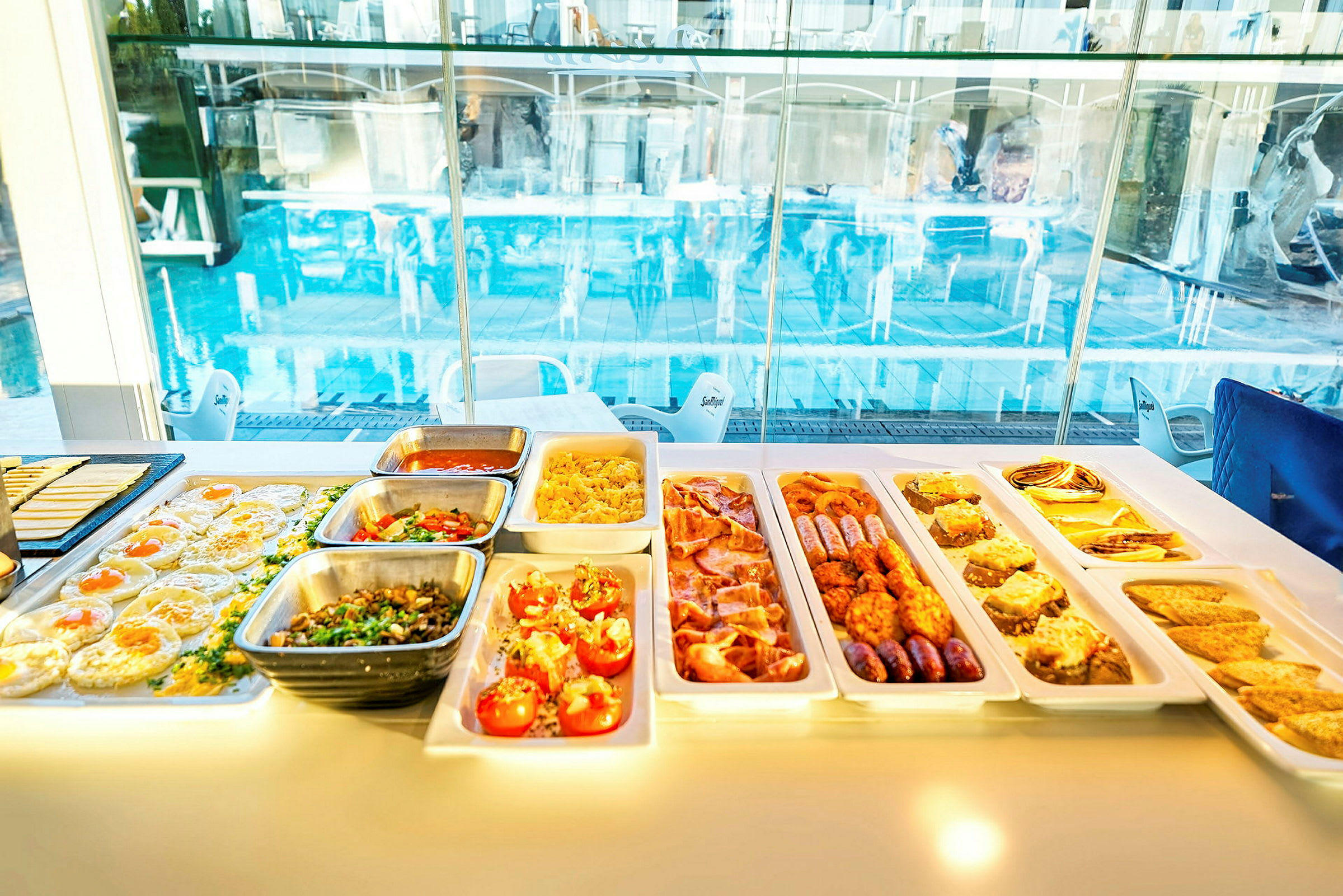 Buffet, jossa on erilaisia ruokia ikkunan äärellä, näkymä uima-altaalle. (Tekoälyn luoma teksti)