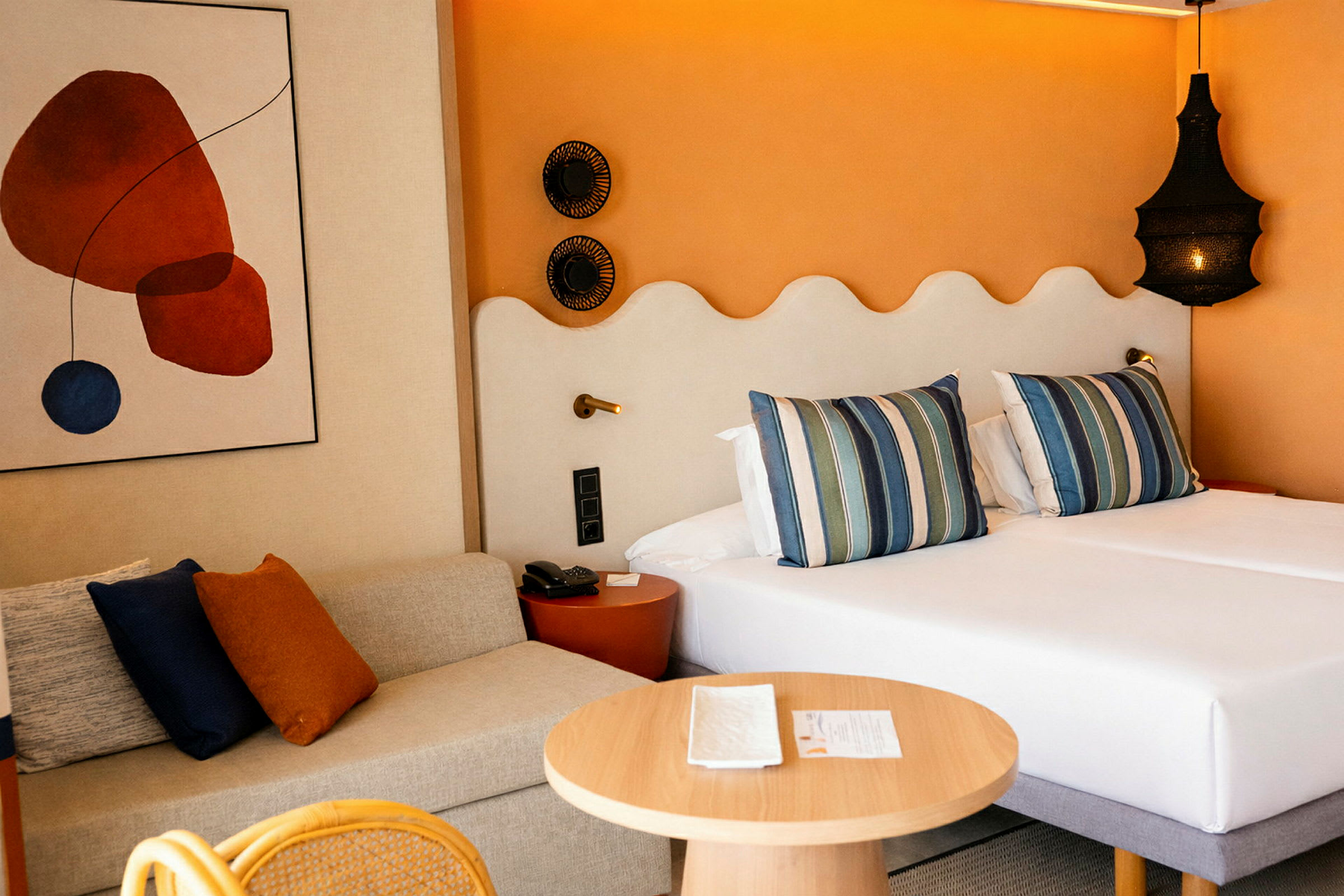 Hotellihuone, jossa on kaksi vuodetta, sohva ja pyöreä puupöytä vieressä. (Tekoälyn luoma teksti)