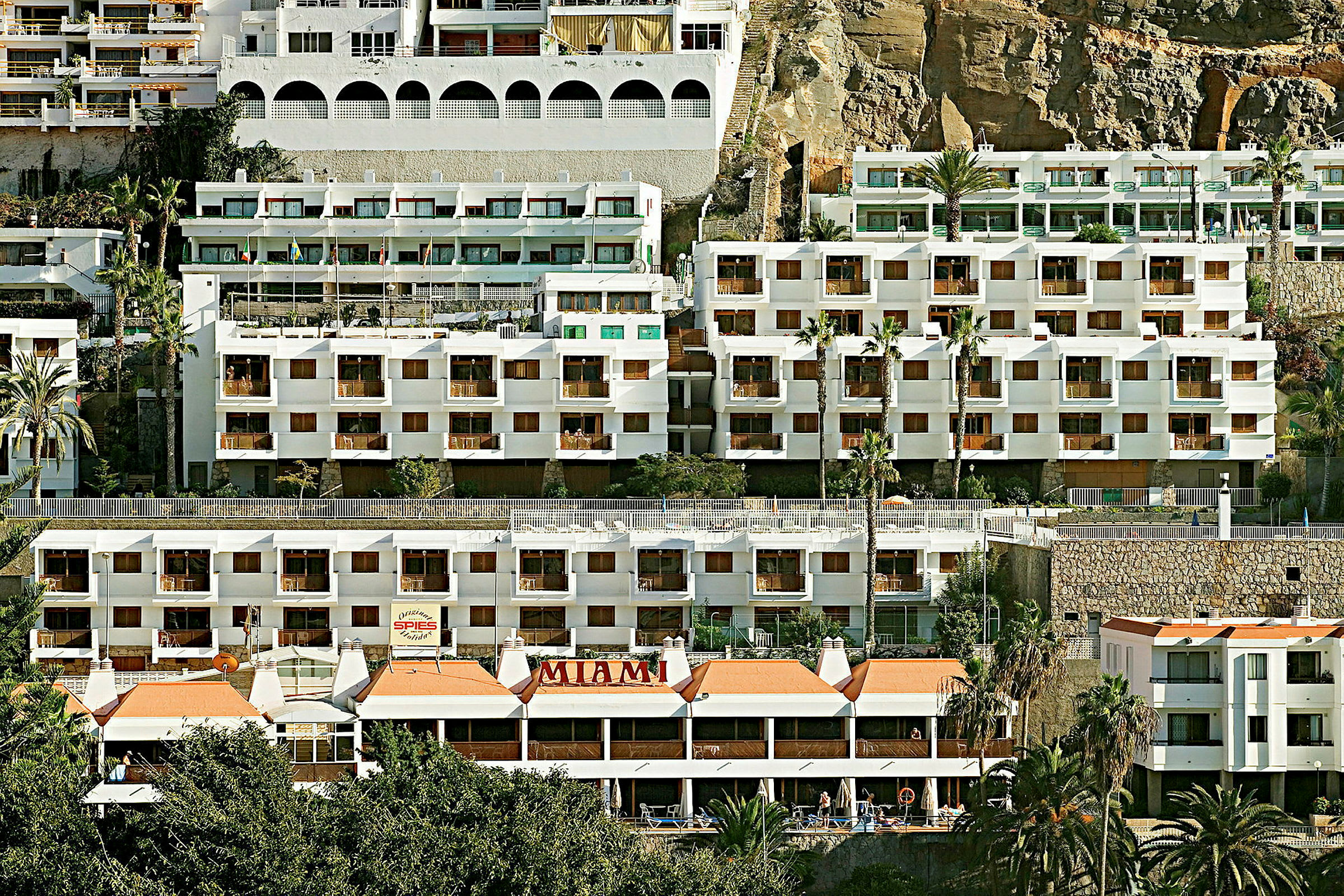 Useita valkoisia parvekkeellisia rakennuksia, jotka on rakennettu vuorenrinteeseen. (Tekoälyn luoma teksti)