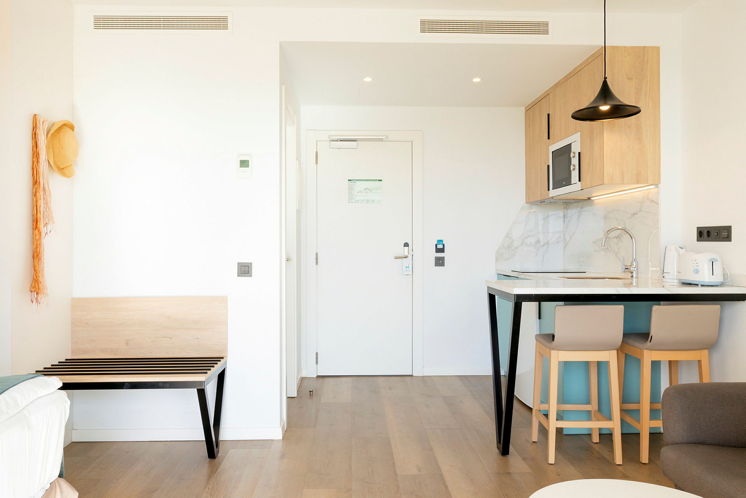 Kuva modernista hotellihuoneesta, jossa keittiötila ja sisäänkäynti. (Tekoälyn luoma teksti)