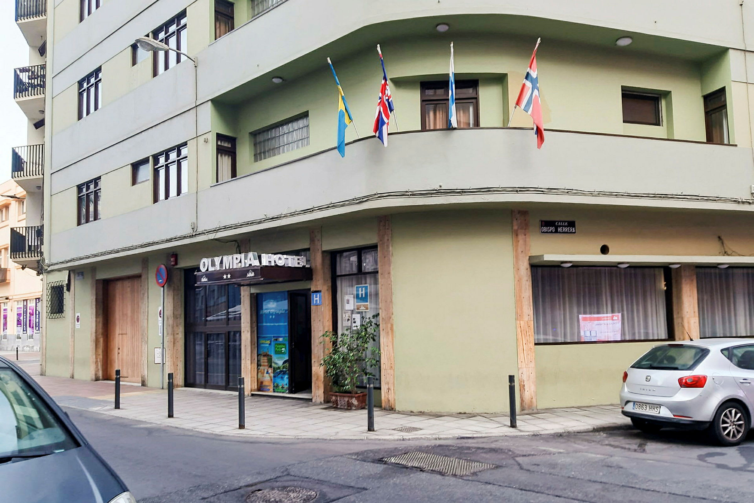 Vihreä rakennus, jonka sisäänkäynnin yläpuolella lukee 'Olympia Hotel'. Useita lippuja on asetettu parvekkeelle. (Tekoälyn luoma teksti)
