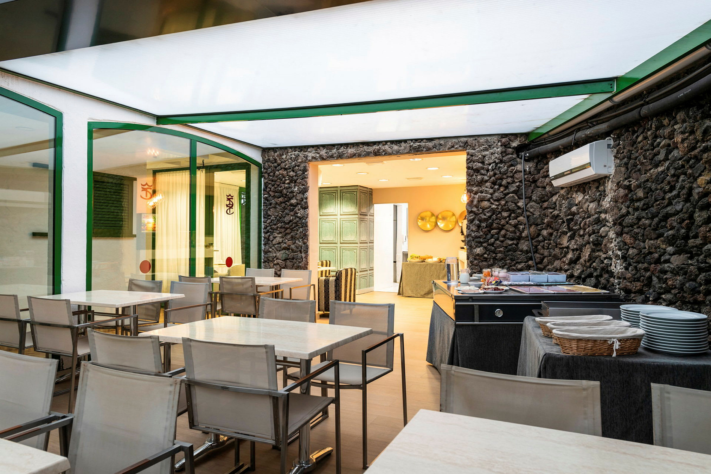 Ruokailutila, jossa on pöytiä ja tuoleja sekä buffet-alue kiviseinän vieressä. (Tekoälyn luoma teksti)