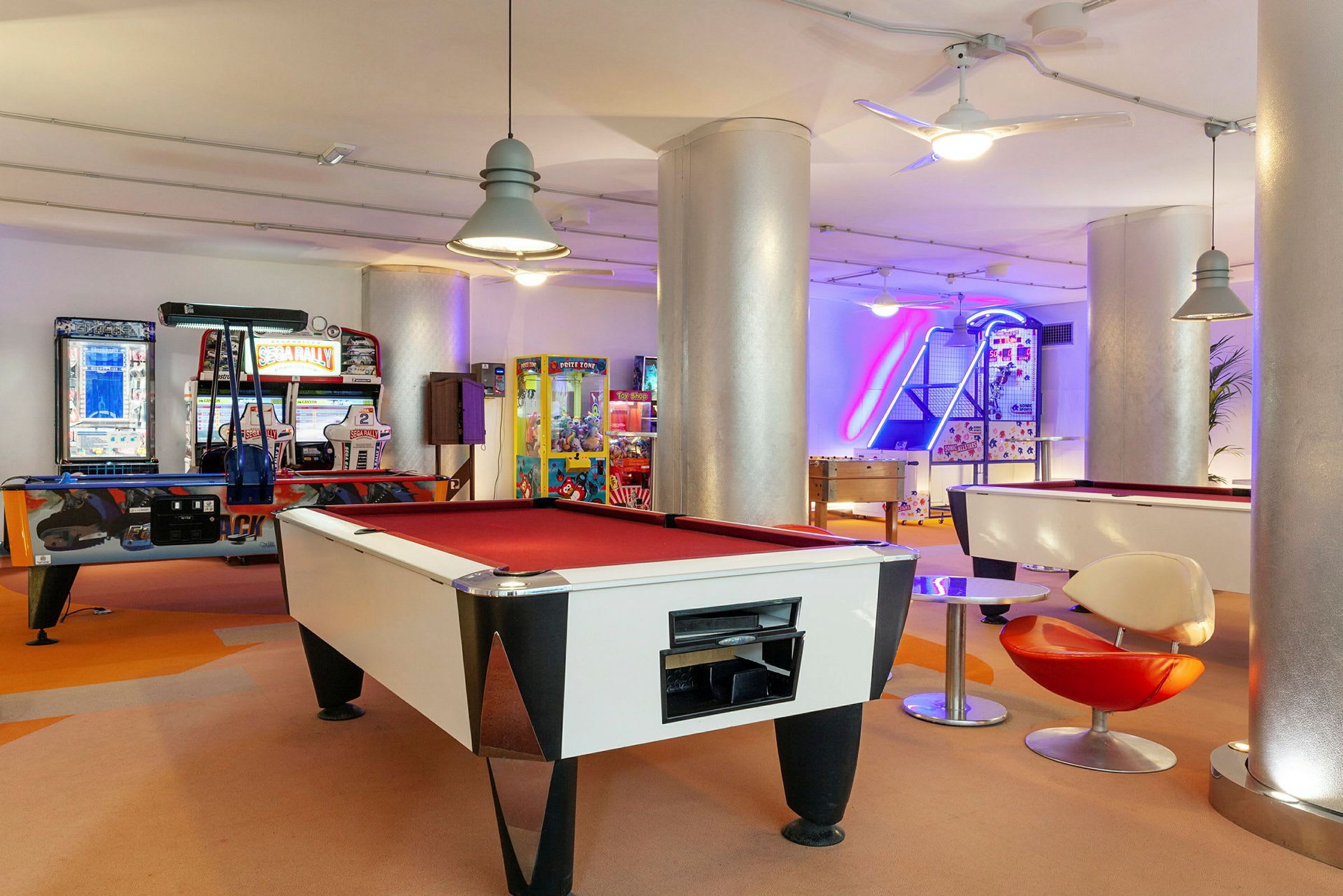 Pelihuone, jossa biljardipöytä, arcade-koneita ja ilmakiekkopelejä. (Tekoälyn luoma teksti)