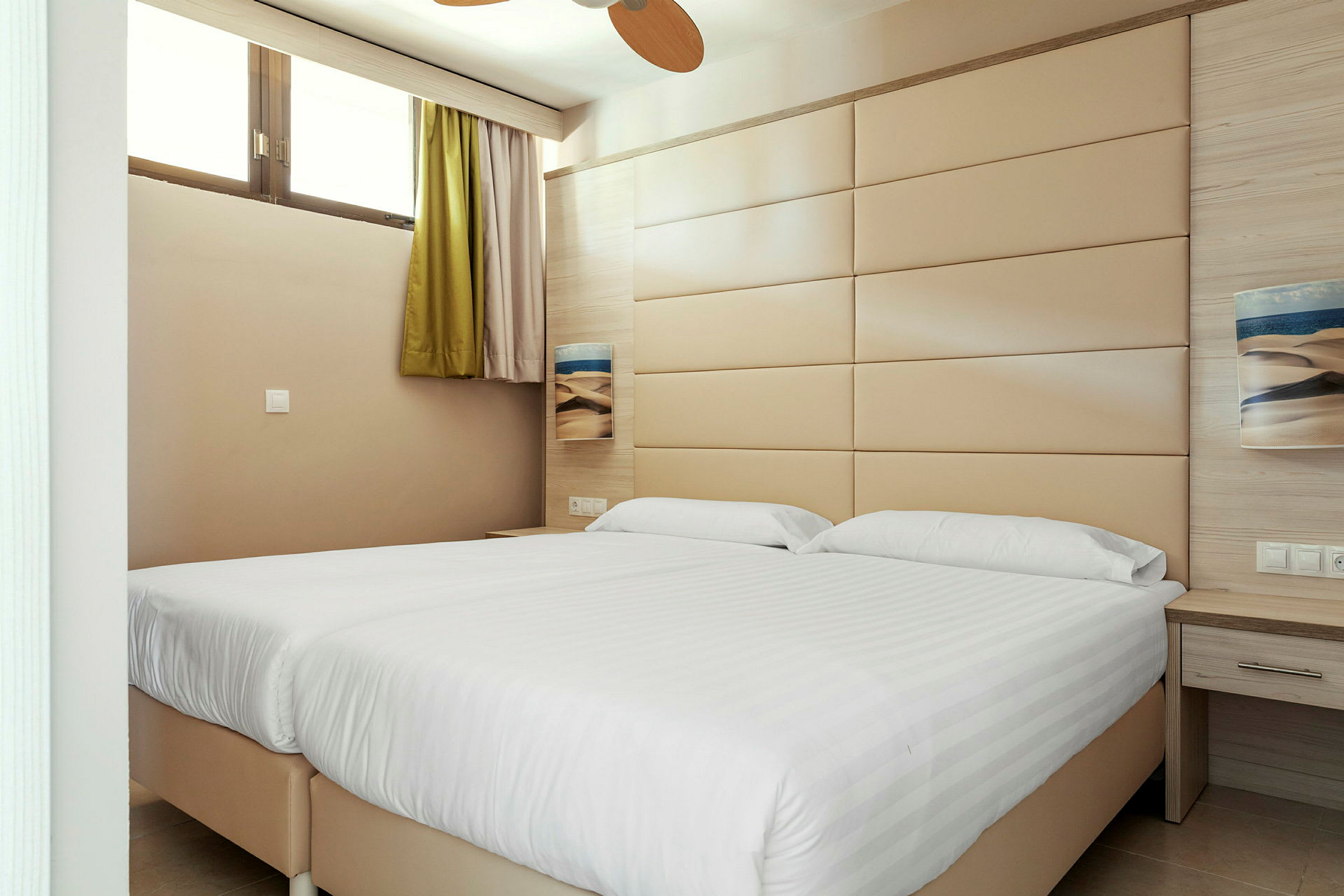 Hotellihuone, jossa on kaksi sänkyä ja beige seinäpaneeli. (Tekoälyn luoma teksti)
