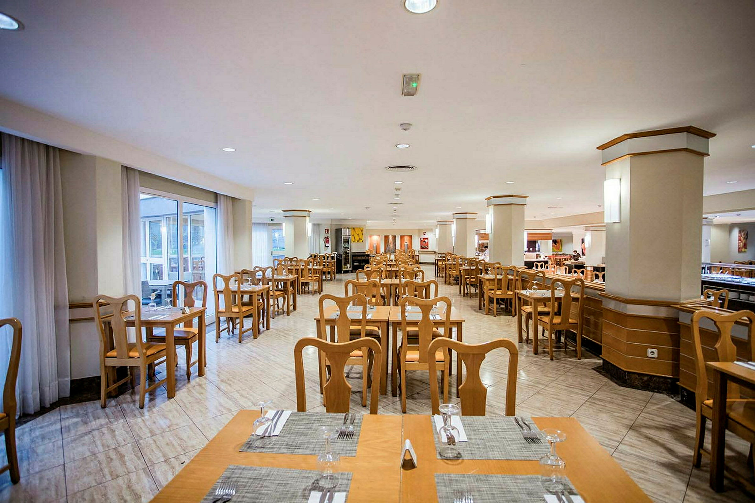 Ravintola, jossa on puiset pöydät ja tuolit sekä pöytäliinoja ja laseja. (Tekoälyn luoma teksti)