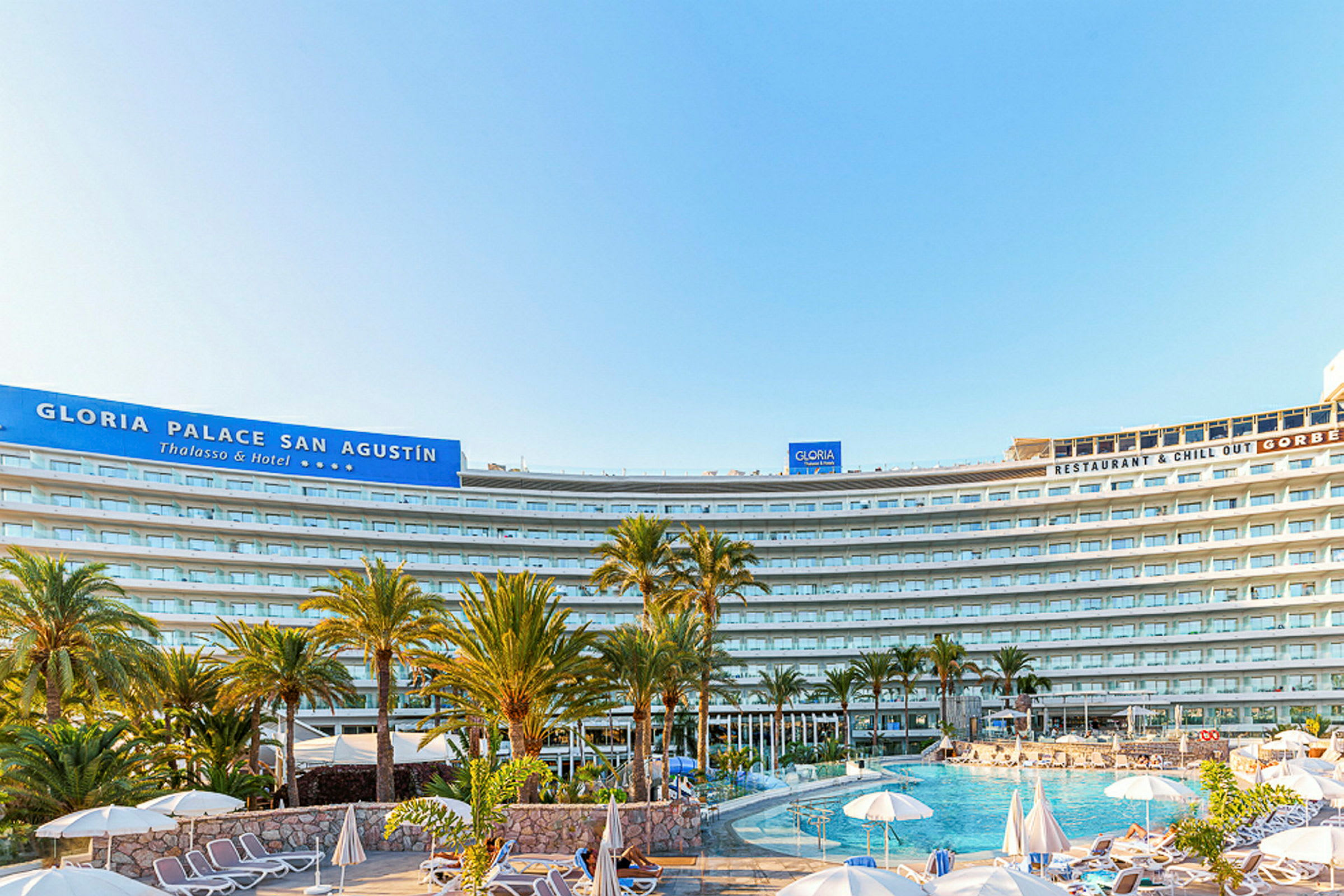 Kuva Gloria Palace San Agustín -hotellista, jossa uima-allas ja aurinkotuoleja etualalla. (Tekoälyn luoma teksti)