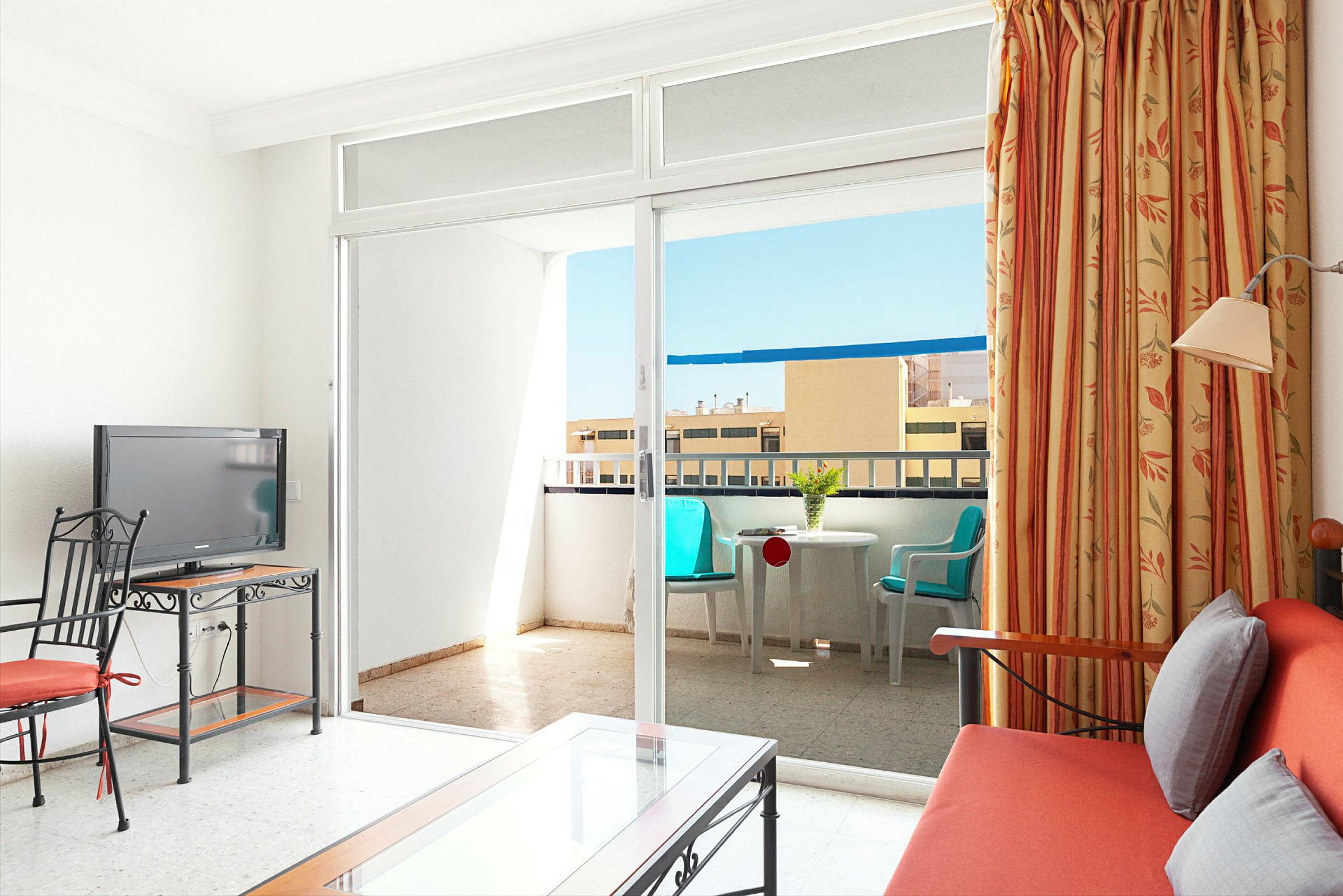 Hotellihuone, jossa on sohva, TV ja pöytä, sekä parveke istuimilla. (Tekoälyn luoma teksti)