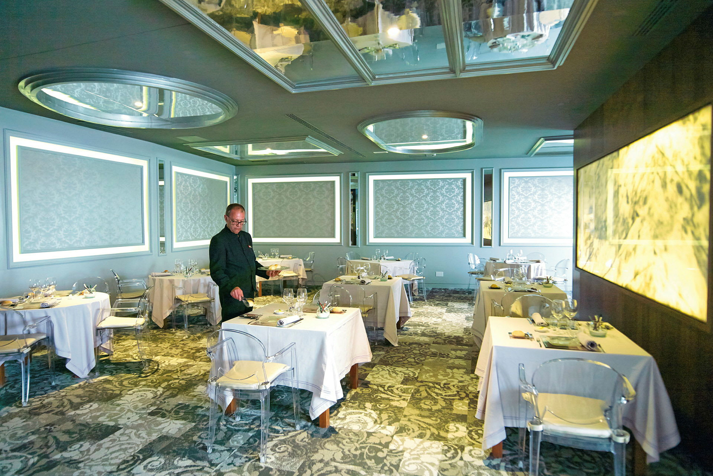 Tyylikäs ravintola, jossa pöydät on katettu valkoisilla liinoilla, kuviolliset seinät ja modernit valaistusjärjestelmät. (Tekoälyn luoma teksti)