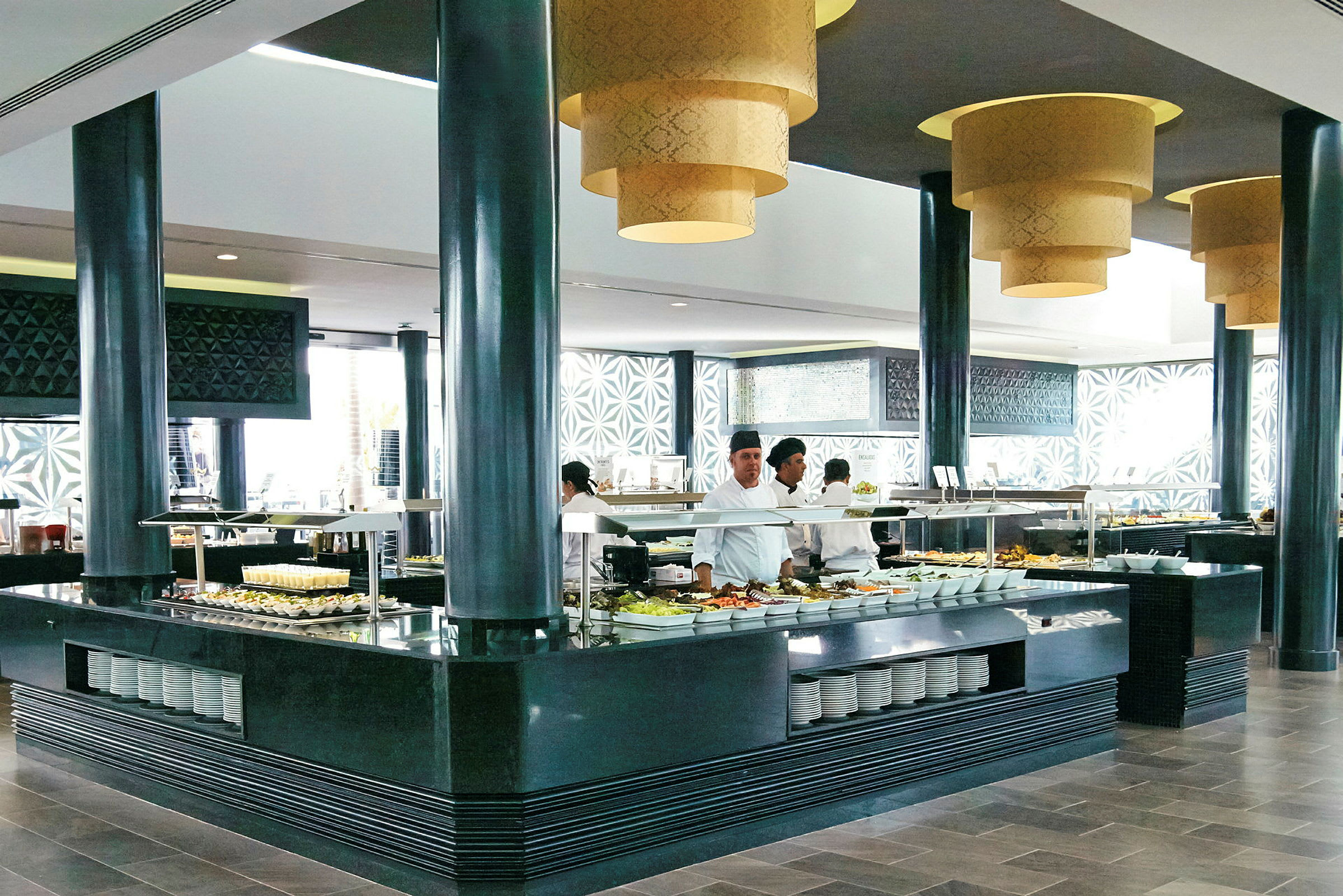 Buffet-alue, jossa pöydät täynnä erilaisia ruokia ja katosta riippuvat koristellut valaisimet. (Tekoälyn luoma teksti)