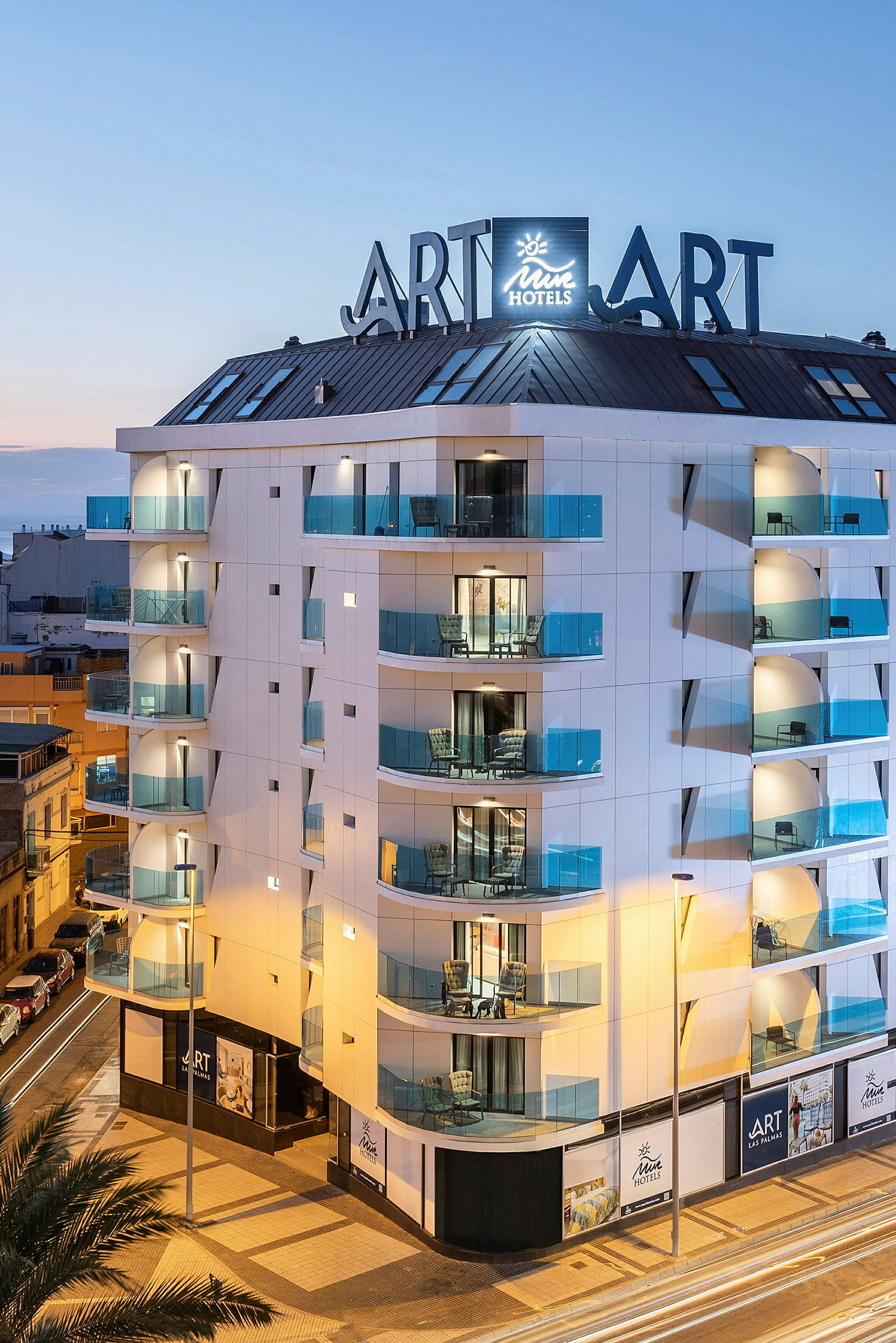 Moderni hotellirakennus, jossa on lasiparvekkeet ja kylttejä iltataivaan alla. (Tekoälyn luoma teksti)