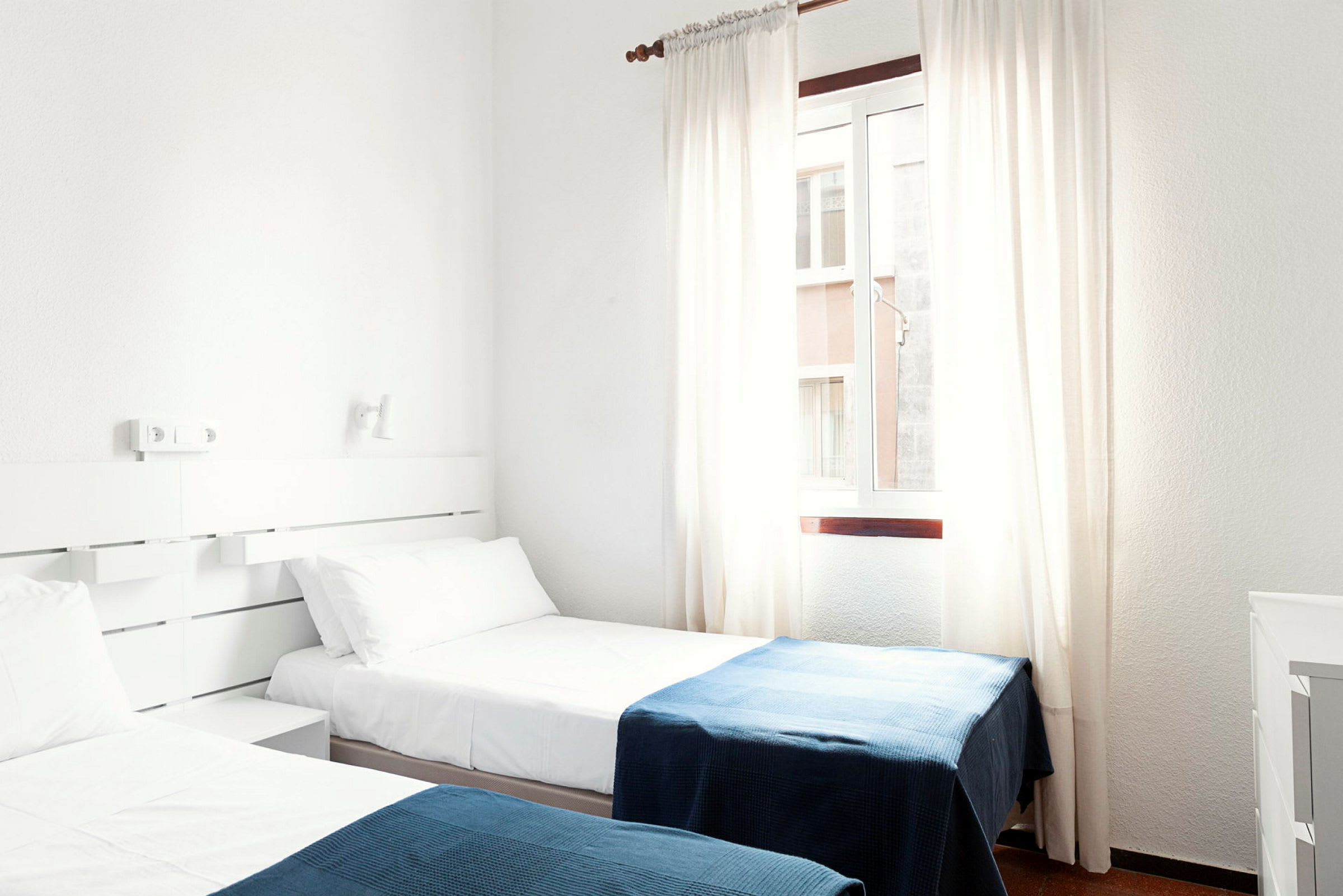 Hotellihuone, jossa on kaksi erillistä vuodetta valkoisilla lakanoilla ja sinisillä vilteillä. (Tekoälyn luoma teksti)