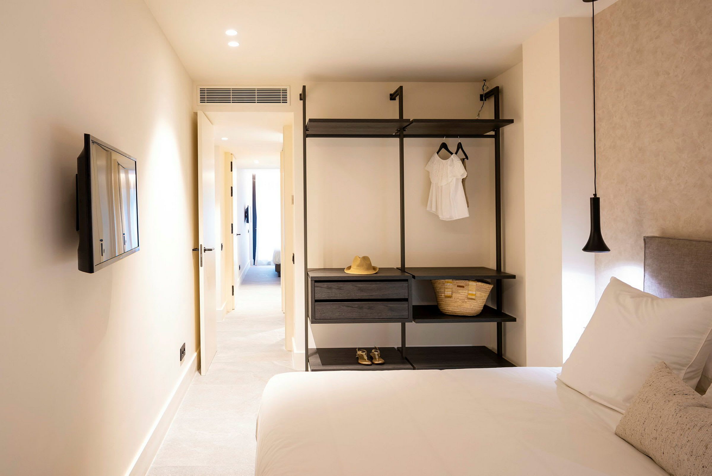 Moderni hotellihuone, jossa sänky, televisio ja avohyllyt. (Tekoälyn luoma teksti)
