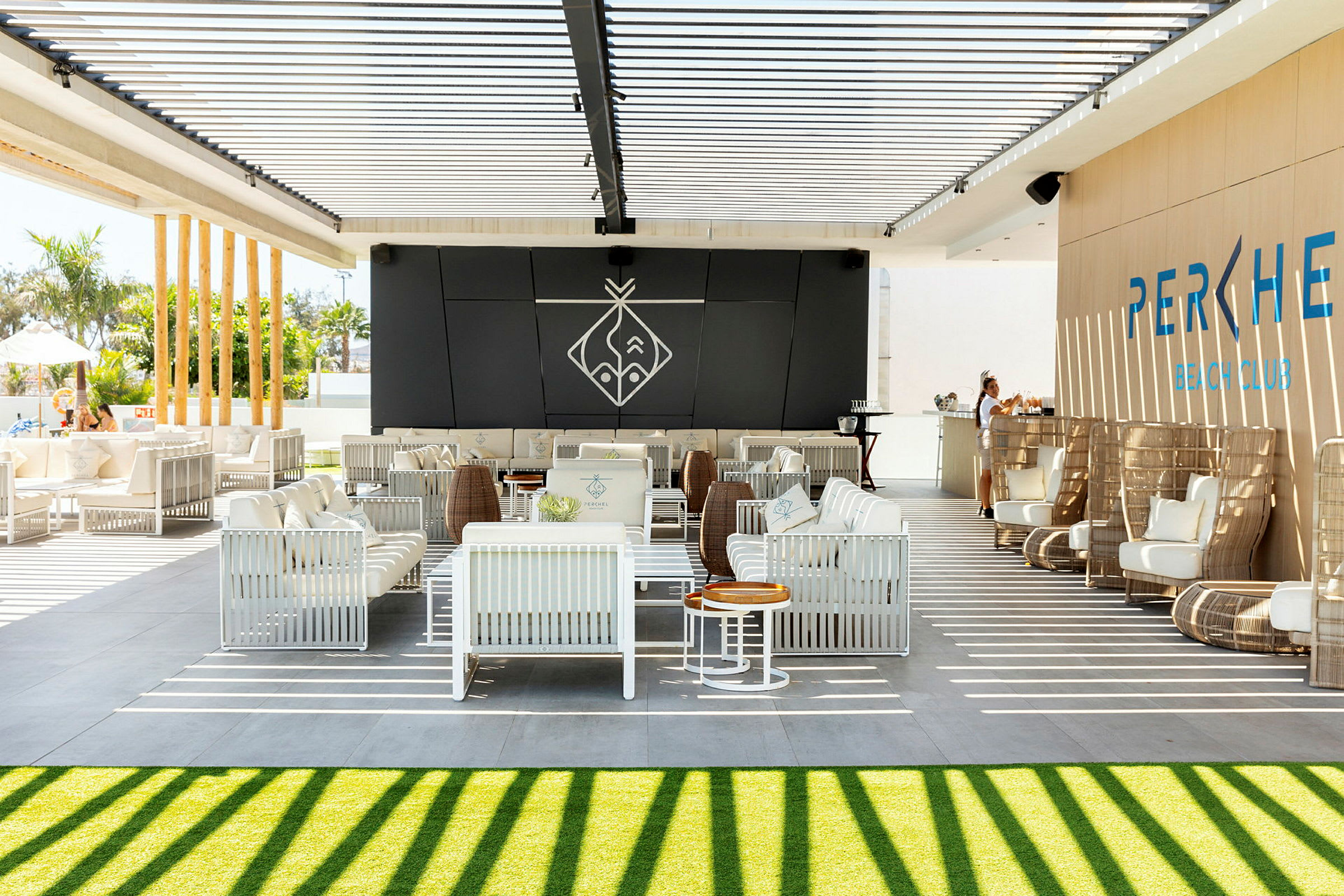 Ulkolounge, jossa on valkoisia istuimia ja baari pergolan alla varjossa. (Tekoälyn luoma teksti)