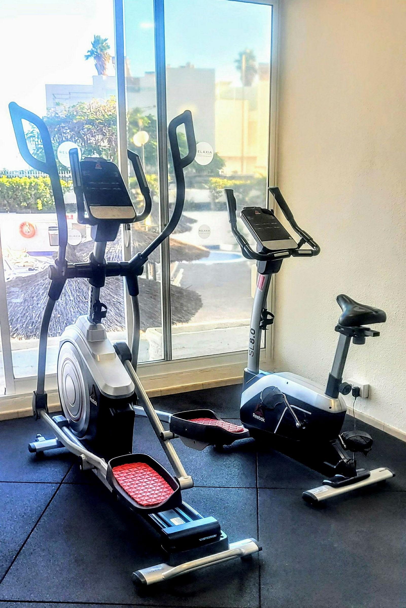 Kuntosali, jossa on cross-trainer ja kuntopyörä ikkunan edessä. (Tekoälyn luoma teksti)