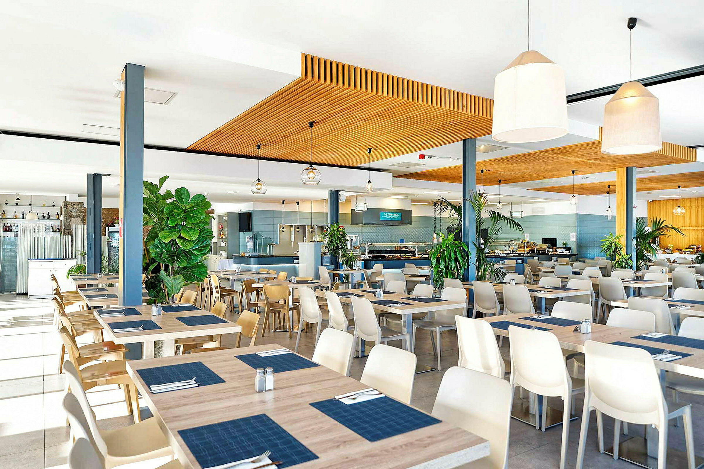 Ravintola, jossa on modernit kalusteet sekä pöytiä ja tuoleja. Koristeena suuria ruukkukasveja. (Tekoälyn luoma teksti)