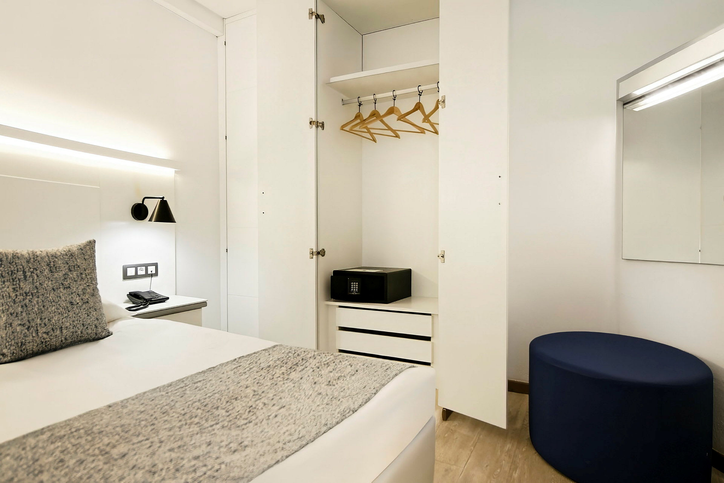 Hotellihuone, jossa avoin vaatekaappi, sänky ja peili. (Tekoälyn luoma teksti)