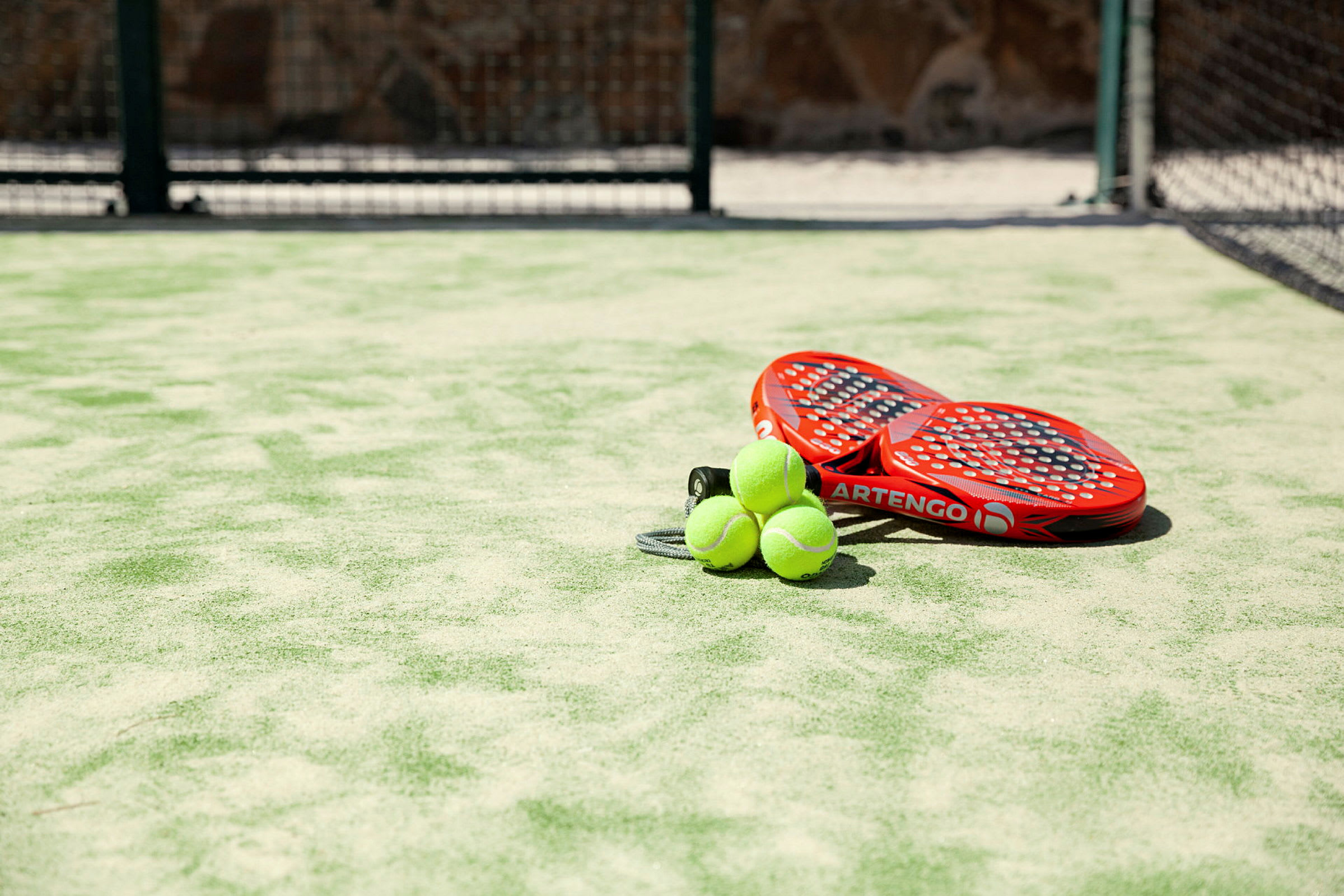 Kaksi punaista padel-mailaa ja kolme vihreää palloa tekonurmikentällä. (Tekoälyn luoma teksti)