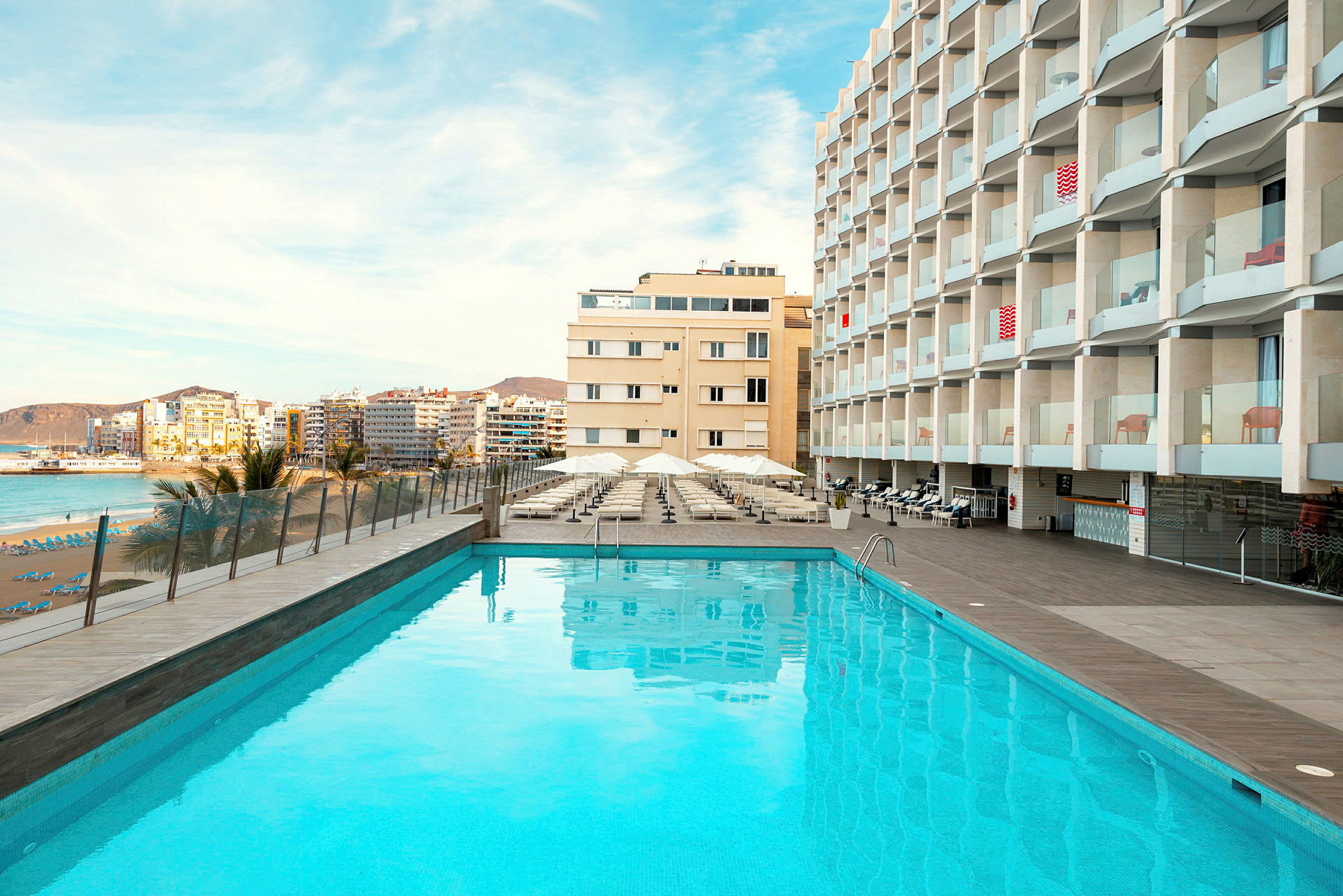 Ulkouima-allas hotellirakennuksen edessä, taustalla ranta ja kaupunki. (Tekoälyn luoma teksti)