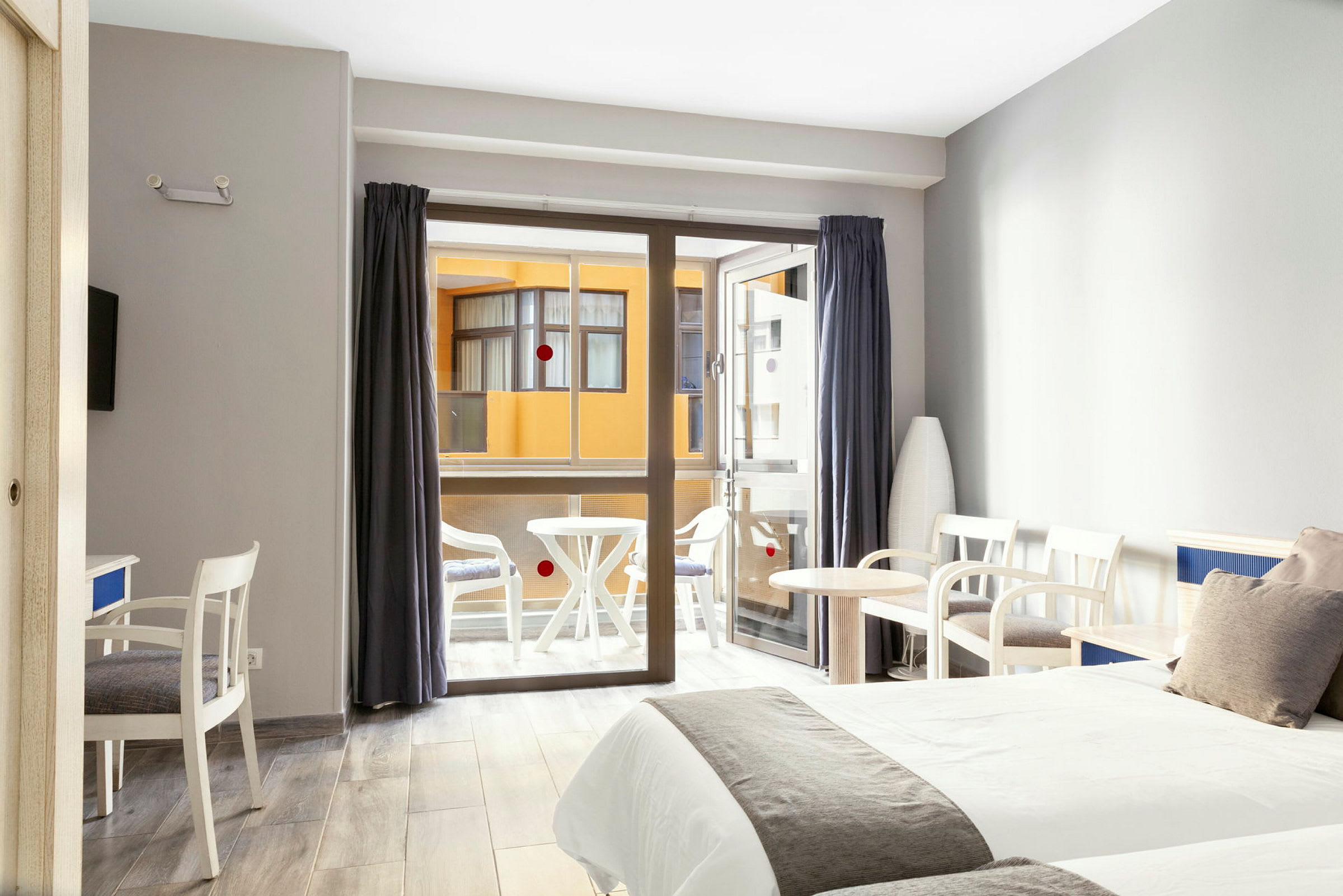Hotellihuone, jossa on kaksi sänkyä, istuinkalusteet ja parveke taustalla. (Tekoälyn luoma teksti)