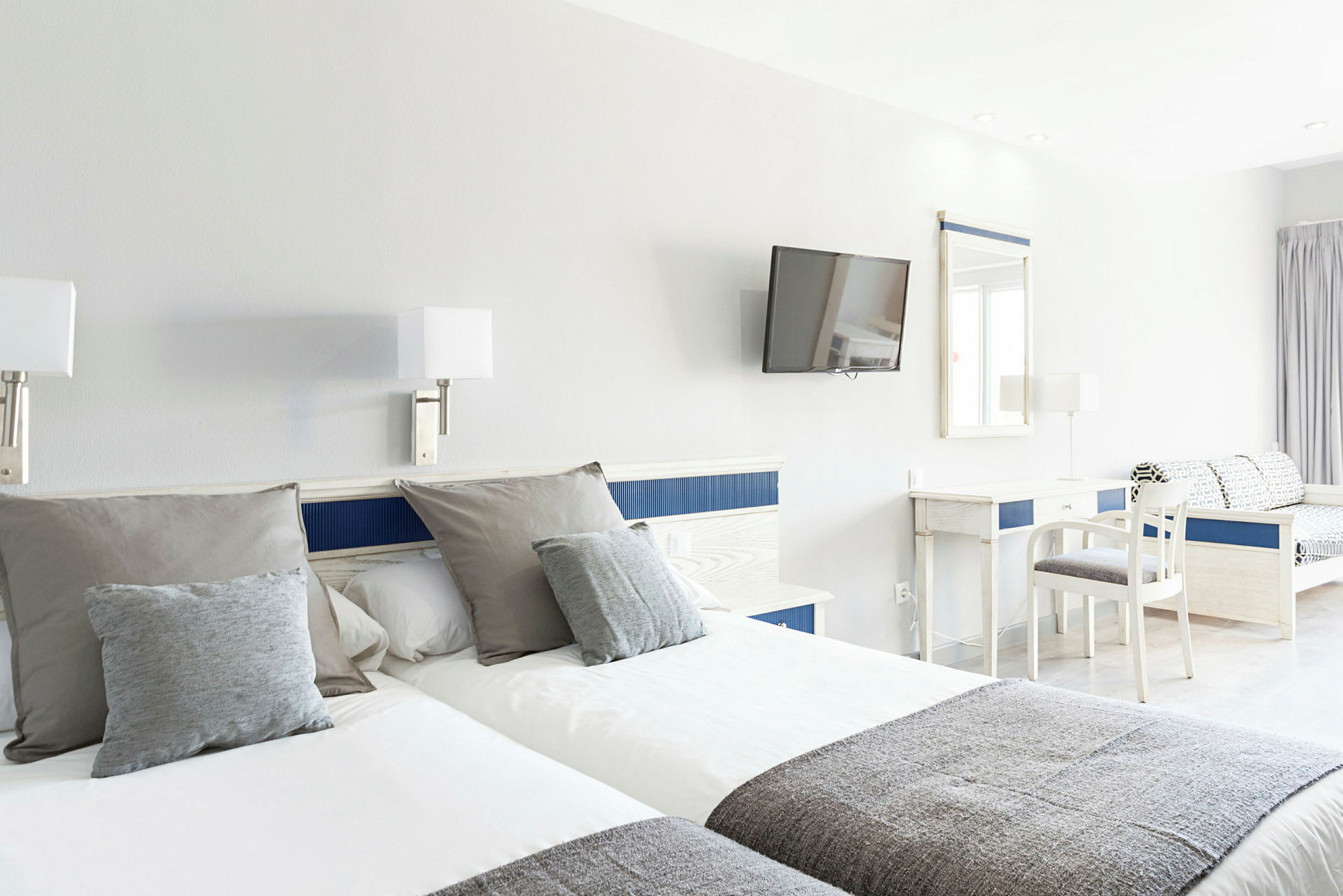 Hotellihuone, jossa kaksi erillistä vuodetta, työpöytä, tuoli ja seinälle kiinnitetty televisio. (Tekoälyn luoma teksti)