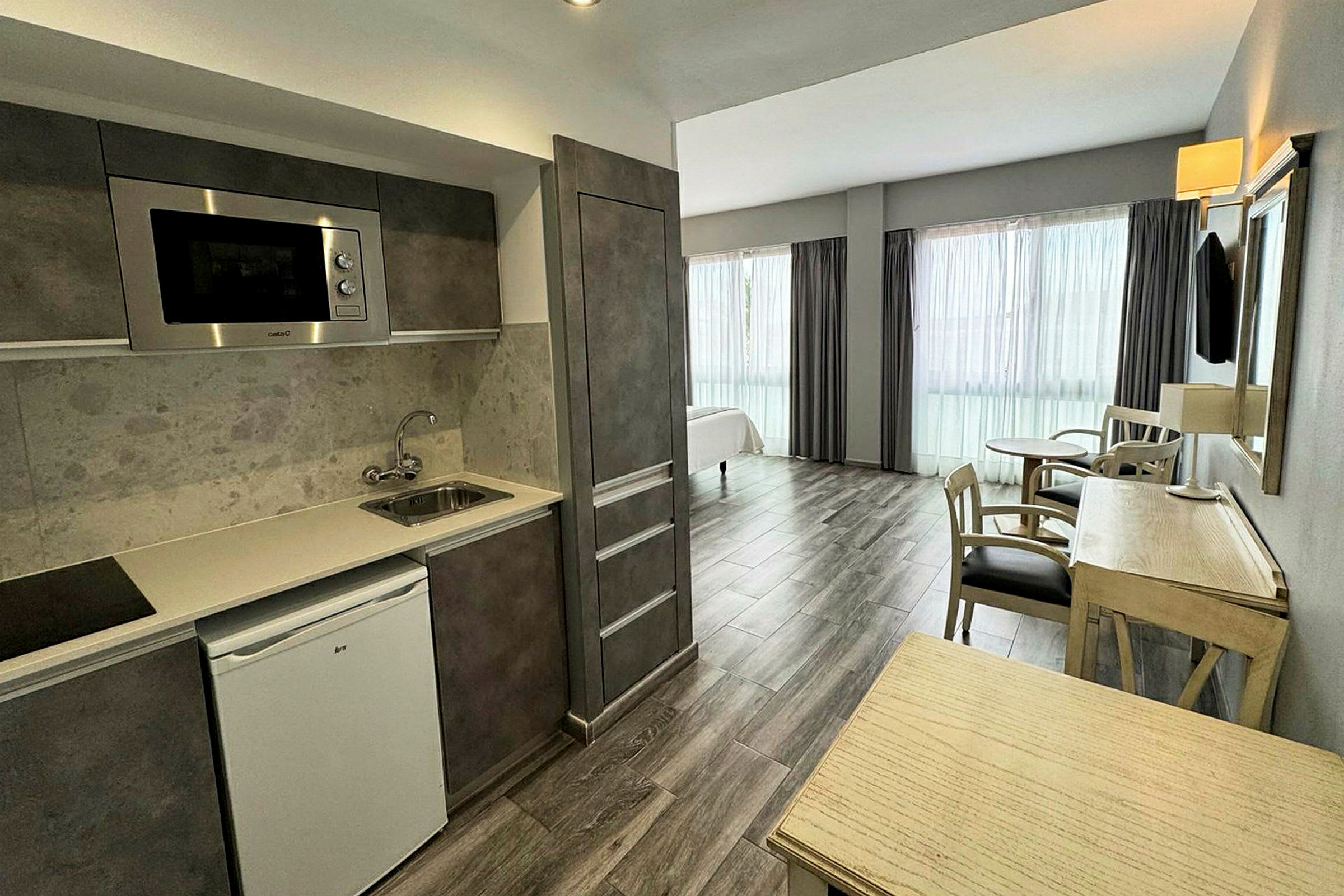 Hotellihuone, jossa on keittiö ja oleskelualue, kalustettu puupöydillä ja tuoleilla. (Tekoälyn luoma teksti)