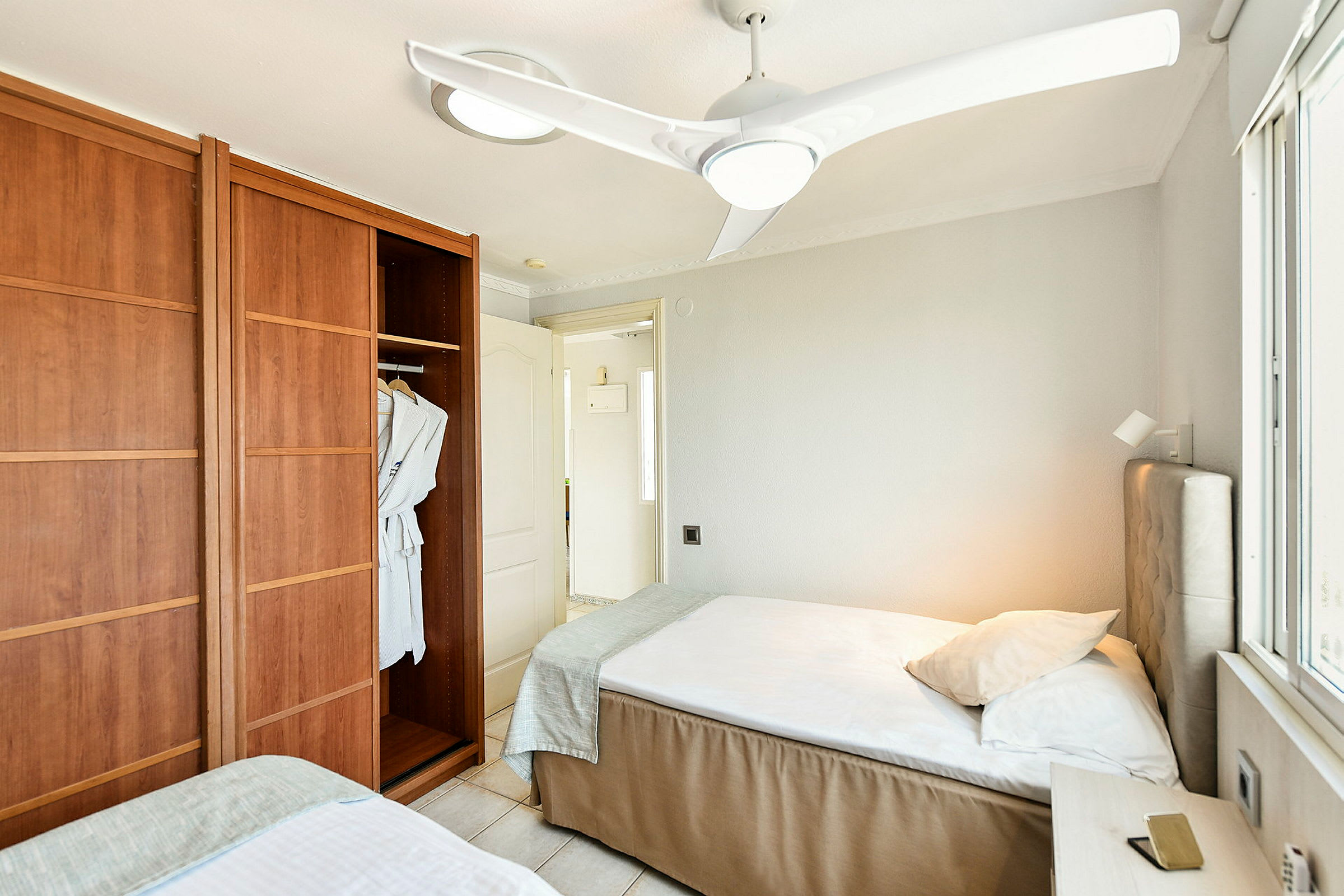 Hotellihuone, jossa kaksi yhden hengen sänkyä, vaatekaappi kylpytakeilla ja kattohylly. (Tekoälyn luoma teksti)