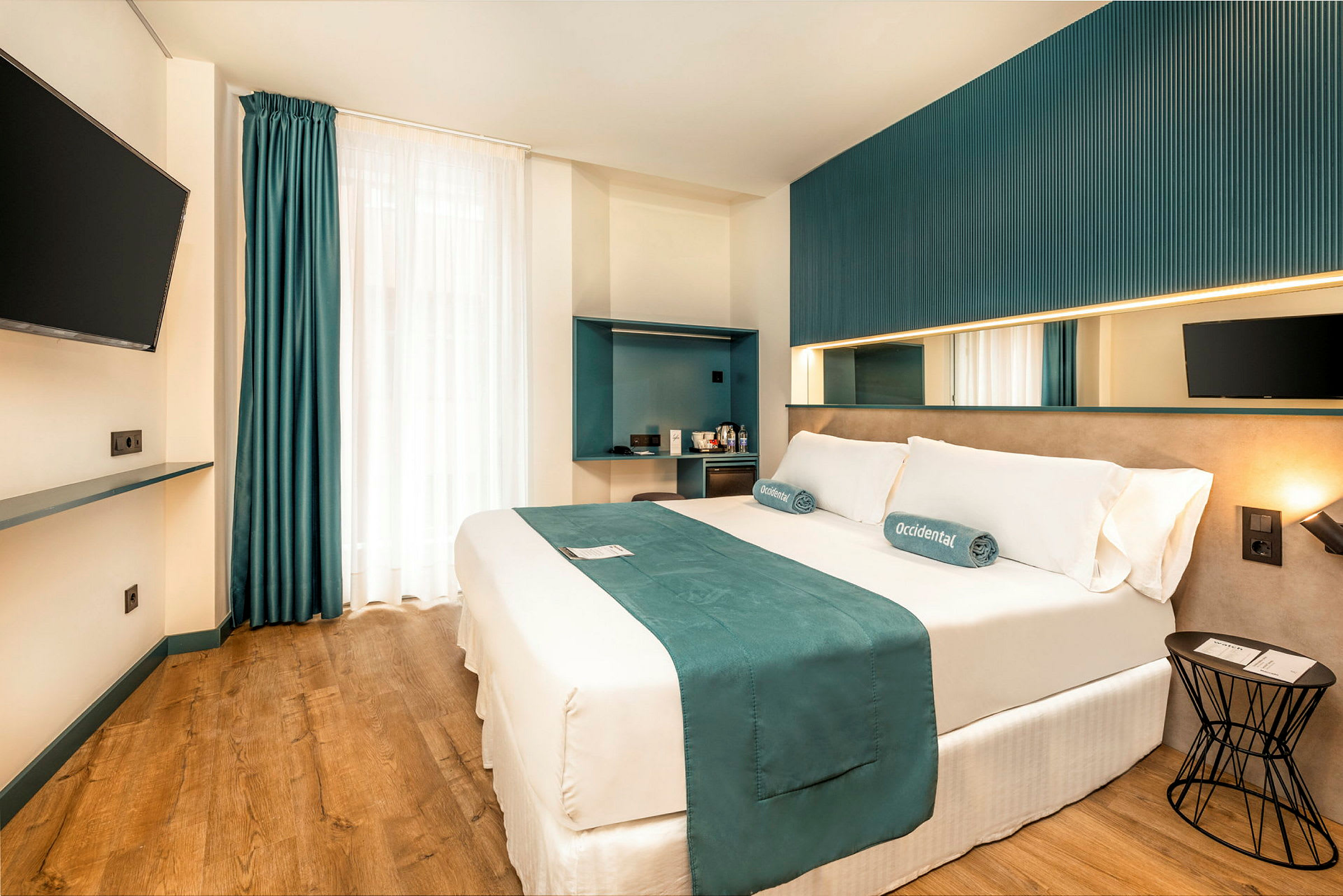 Moderni hotellihuone, jossa on parivuode, seinälle kiinnitetty televisio ja minimalistinen sisustus. (Tekoälyn luoma teksti)