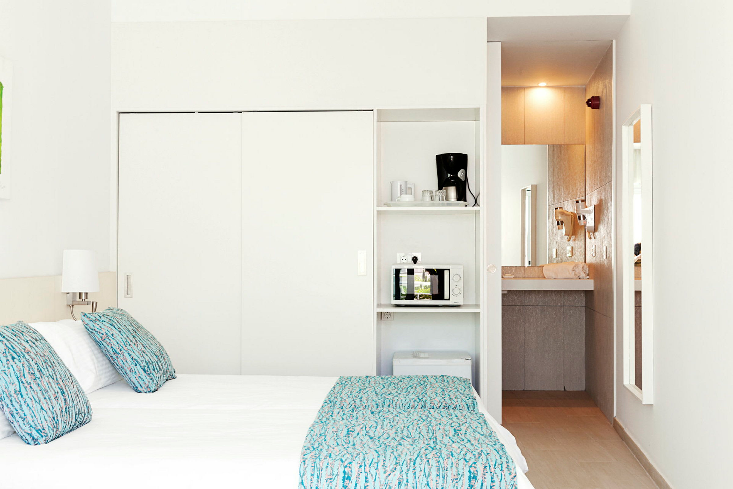 Hotellihuone, jossa on sänky, lamput ja minikeittiö, johon kuuluu mikroaaltouuni ja kahvinkeitin. (Tekoälyn luoma teksti)