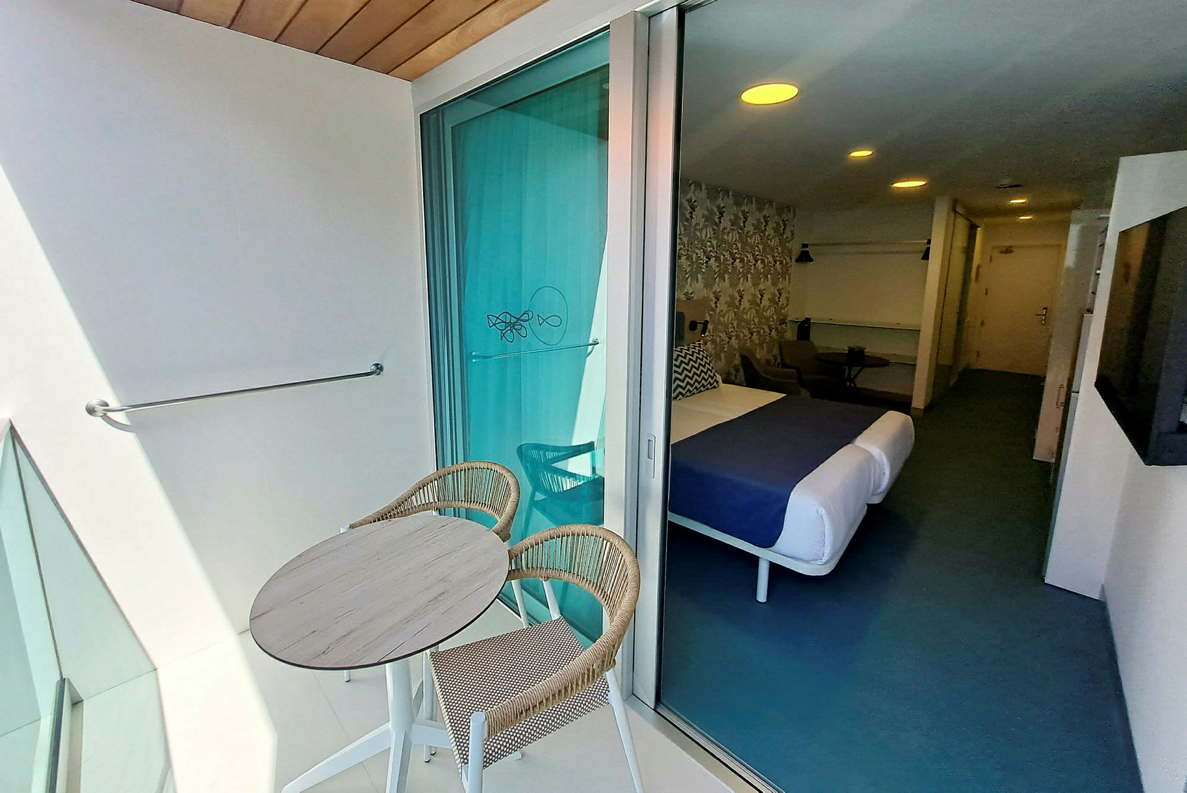 Kuva hotellihuoneesta, jossa on parveke. Parvekkeella on pyöreä pöytä ja kaksi tuolia. (Tekoälyn luoma teksti)