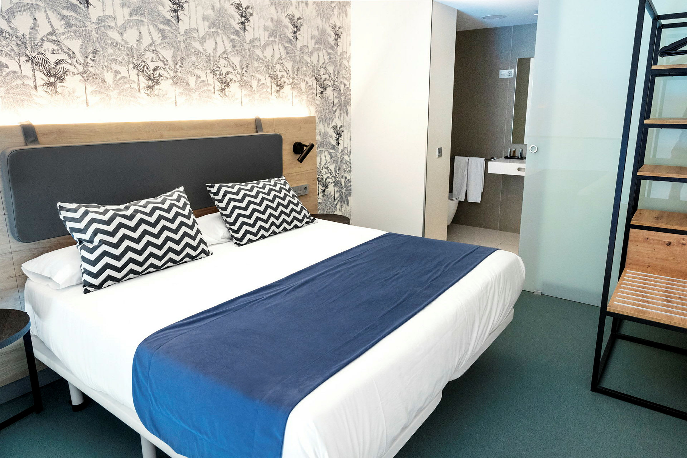 Moderni hotellihuone, jossa on parivuode, sininen päiväpeitto ja kaksi kuviollista tyynyä. (Tekoälyn luoma teksti)