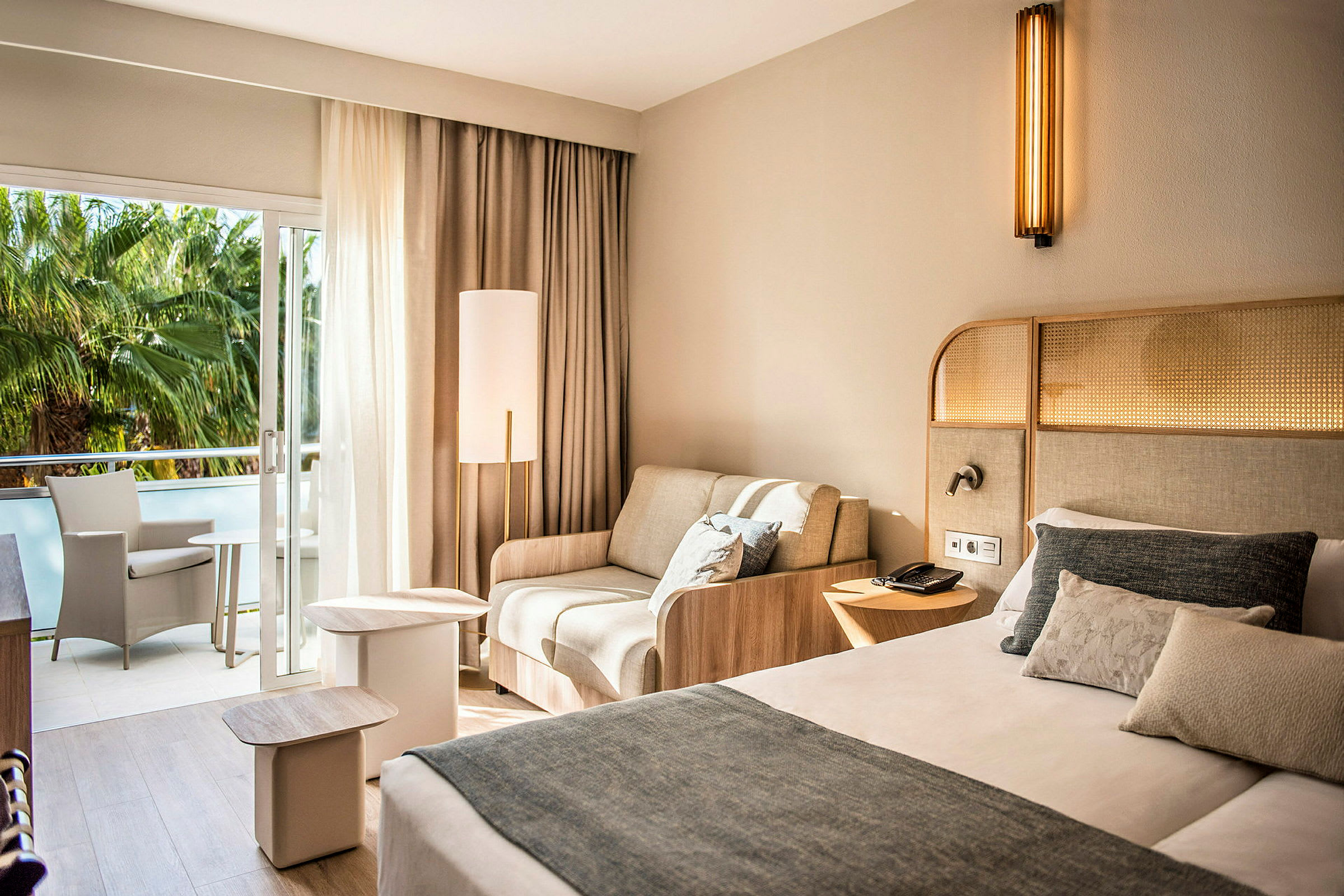 Hotellihuone, jossa on sänky, sohva ja parveke istuinkalusteineen. (Tekoälyn luoma teksti)