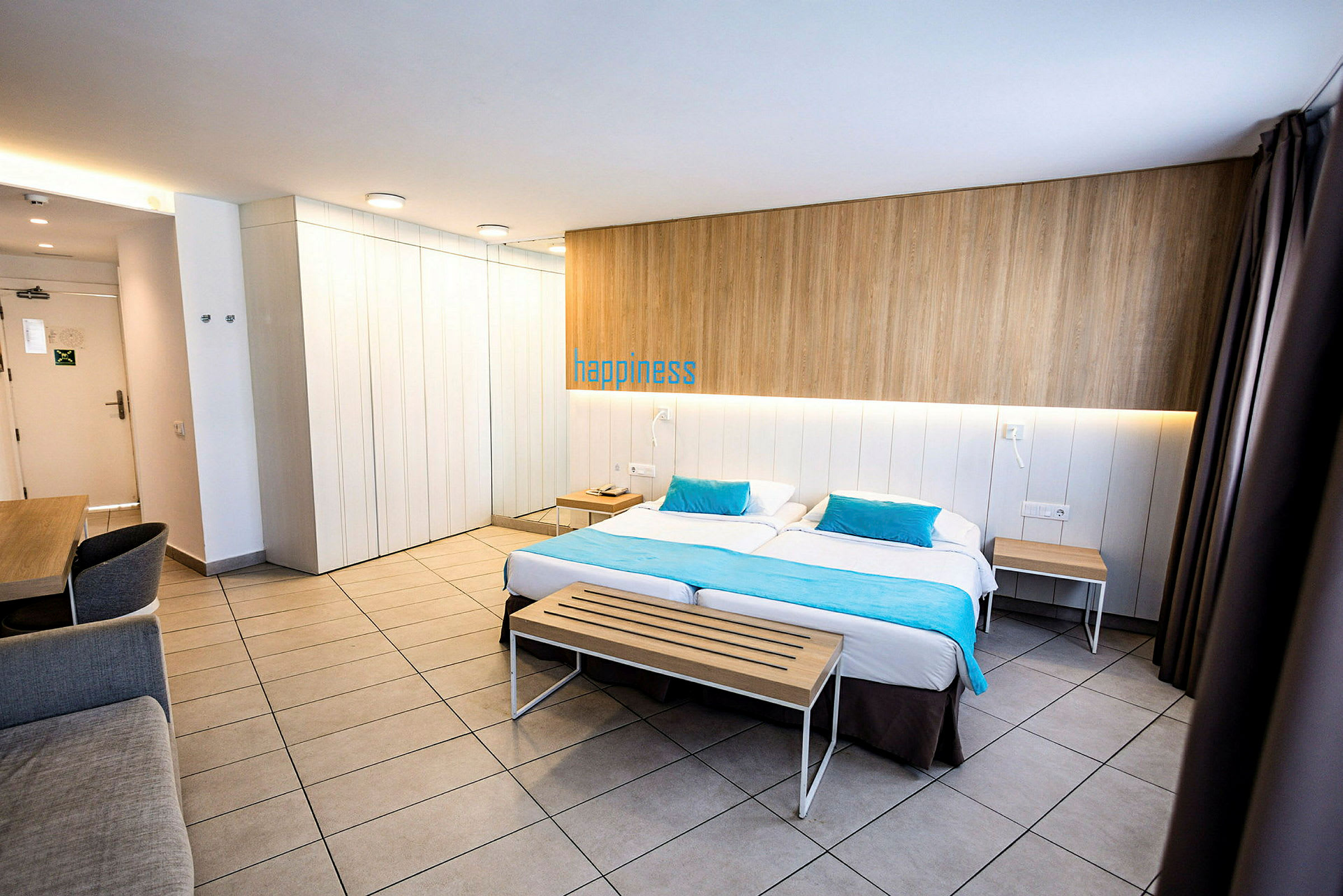 Moderni hotellihuone, jossa on parisänky, puupenkki jalkopäässä ja työpöytä nurkassa. (Tekoälyn luoma teksti)
