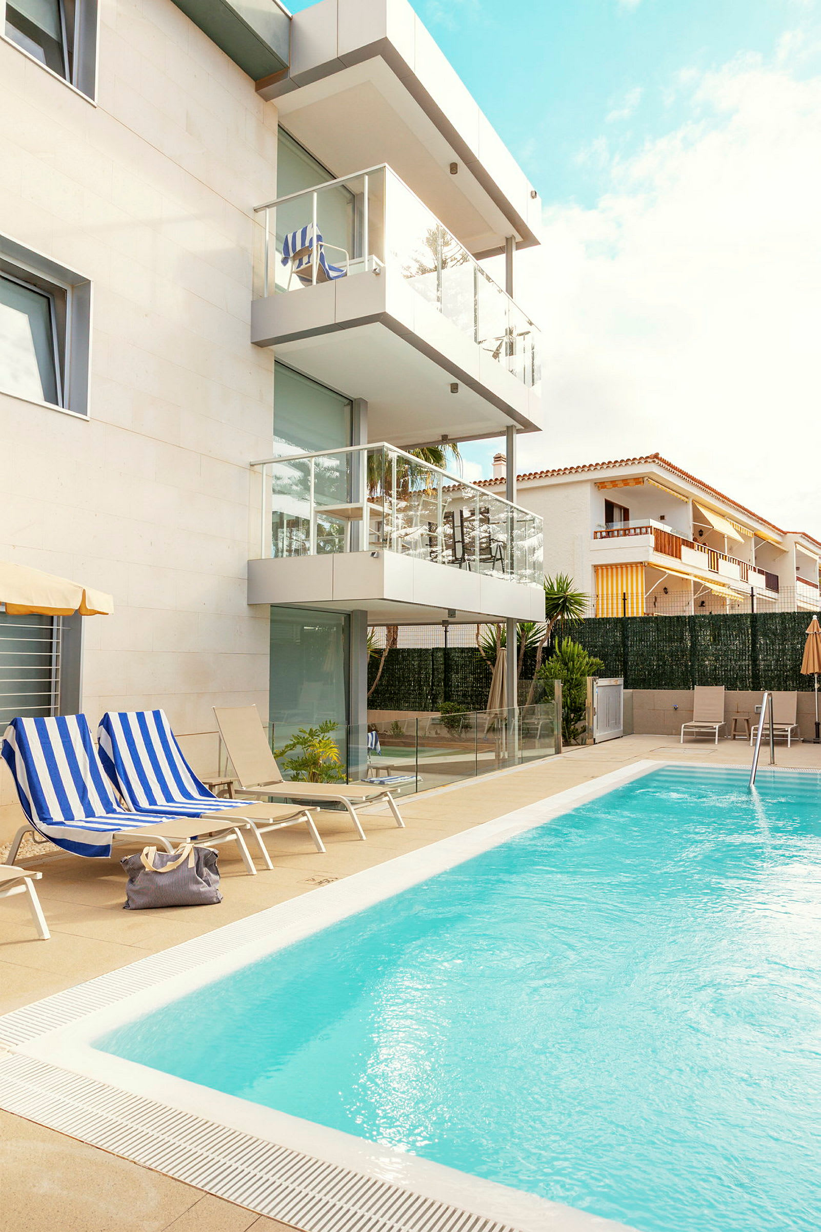 Kuva uima-altaasta modernin rakennuksen vieressä, jossa on parvekkeita, aurinkotuoleja ja sininen taivas. (Tekoälyn luoma teksti)