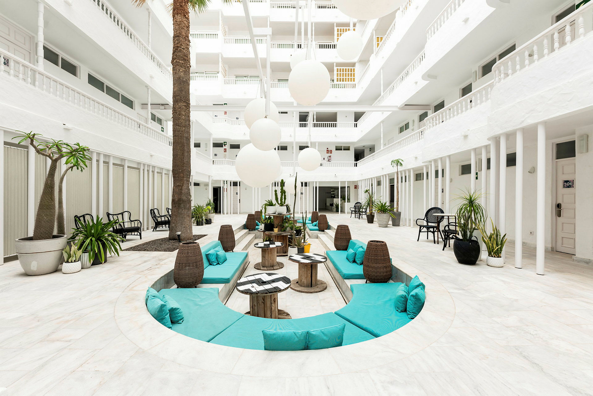 Vaalea atrium, jossa on valkoiset seinät, vihreitä kasveja ja istuinryhmiä turkooseilla tyynyillä. (Tekoälyn luoma teksti)