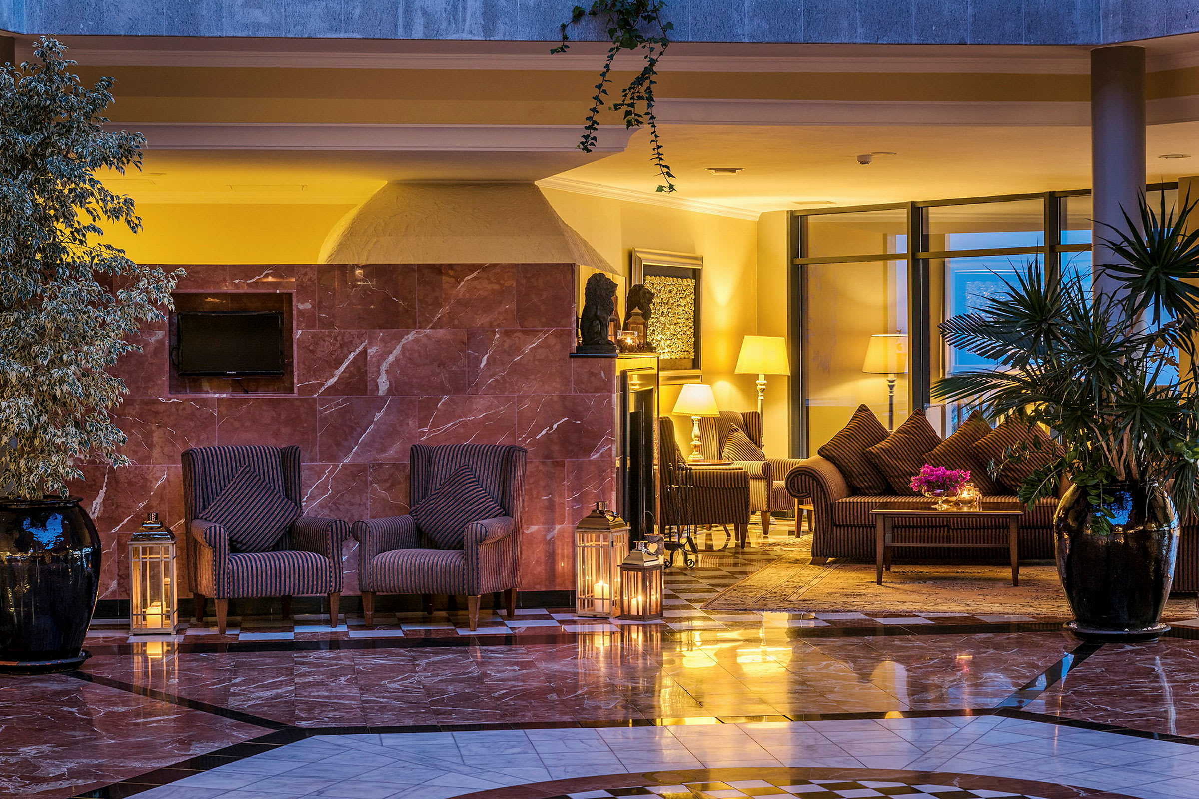 Hotellihuone, jossa on tyylikäs sisustus, mukaan lukien nojatuoleja, pöytiä, lampunvarjostimia ja kasveja. (Tekoälyn luoma teksti)