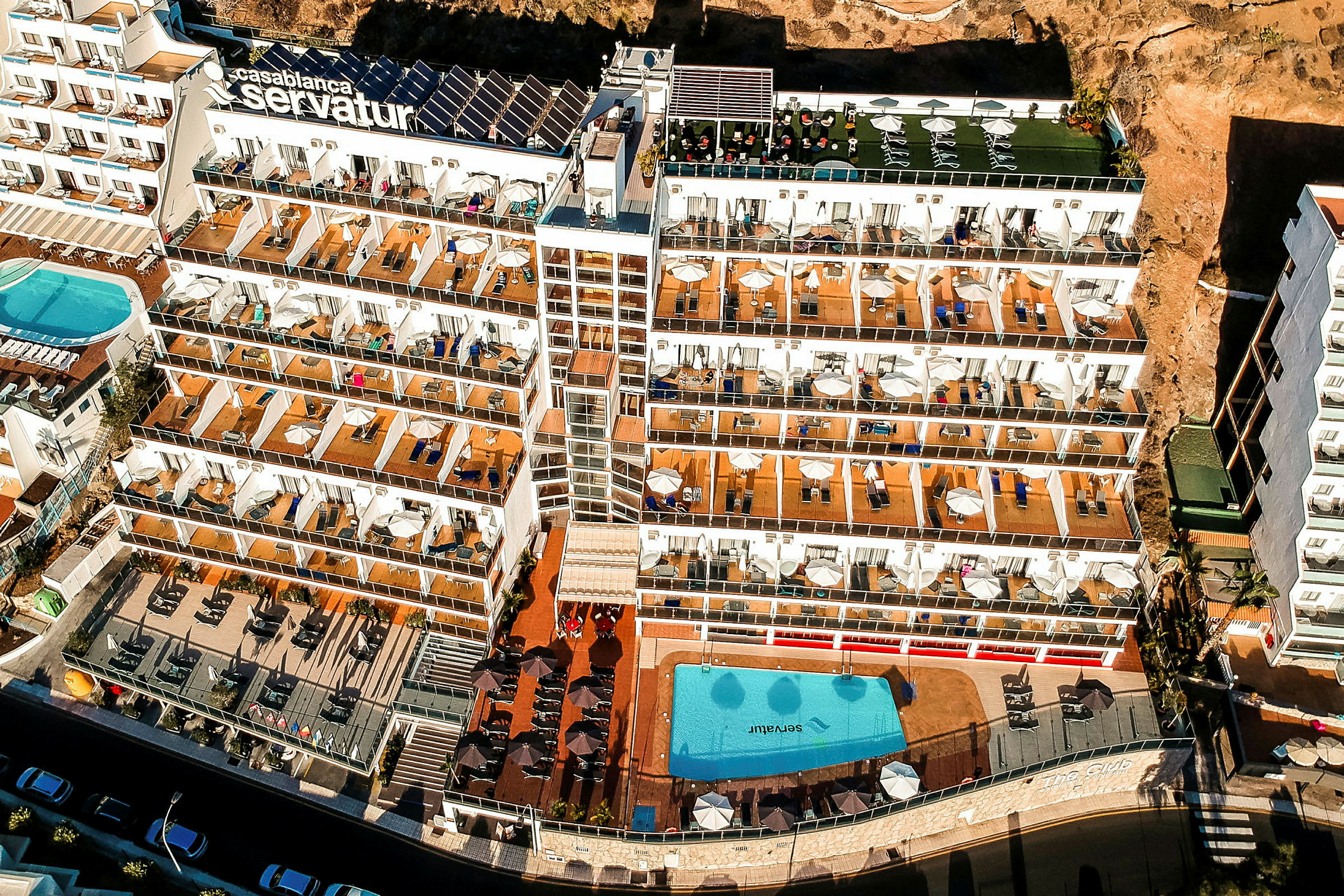 Ilmakuva hotellista, jossa on useita kerroksia, suuret parvekkeet ja uima-allasalue. (Tekoälyn luoma teksti)