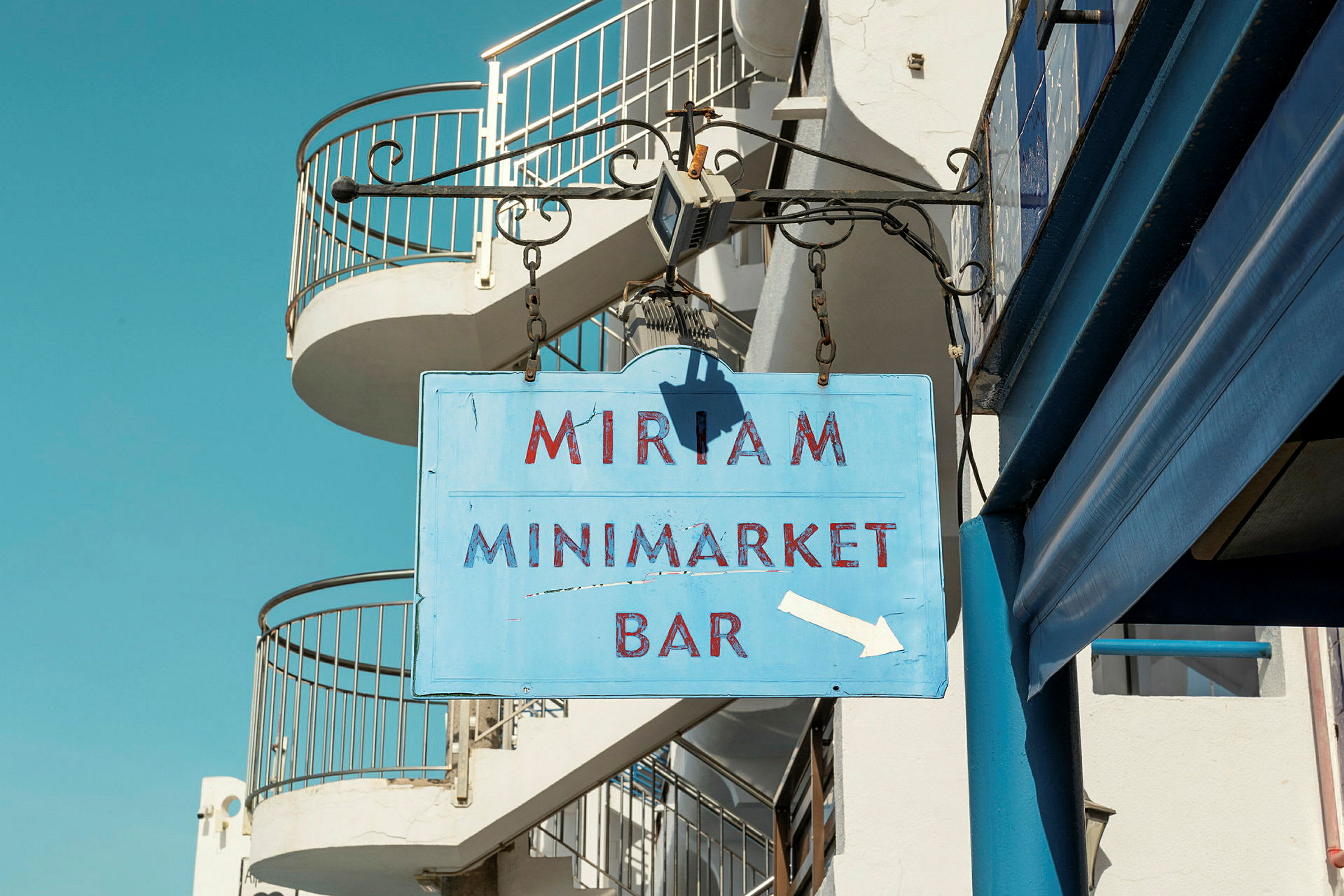 Rakennuksessa roikkuva kyltti, jossa lukee 'Miriam Minimarket Bar'. (Tekoälyn luoma teksti)