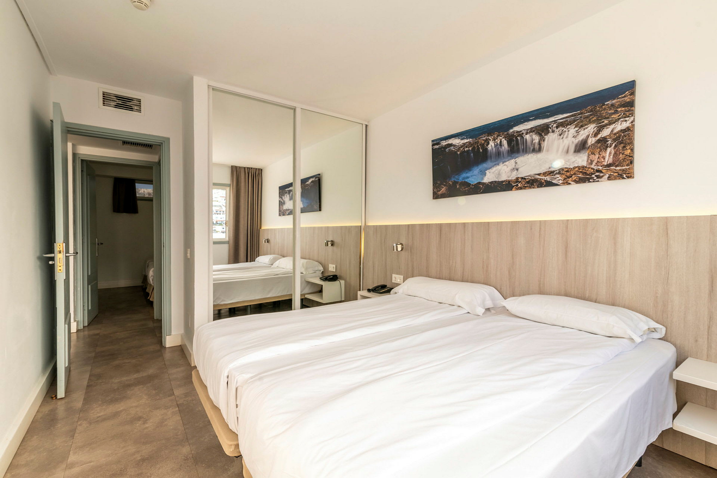 Hotellihuone, jossa on kaksi yhden hengen vuodetta, peiliseinä ja koristeita. (Tekoälyn luoma teksti)