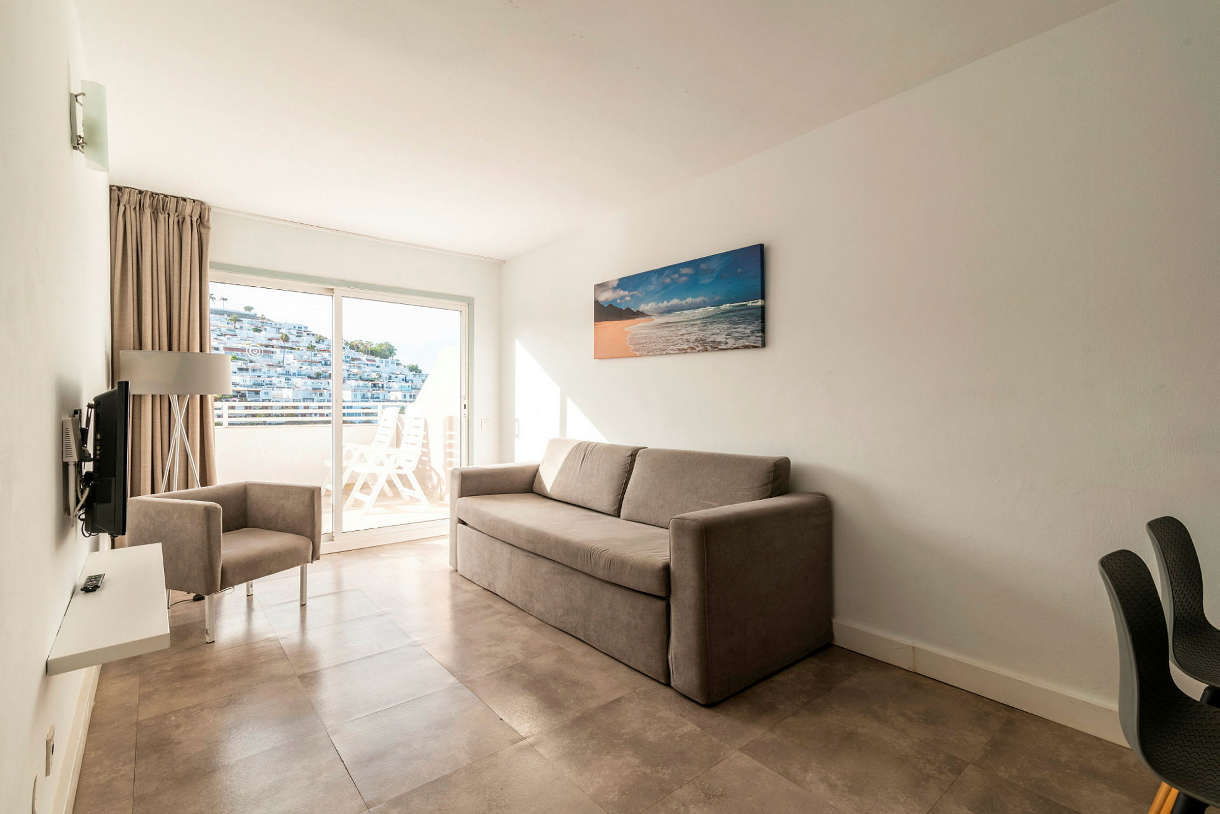 Hotellihuone, jossa on beige sohva ja nojatuoli sekä parveke näköalalla. (Tekoälyn luoma teksti)