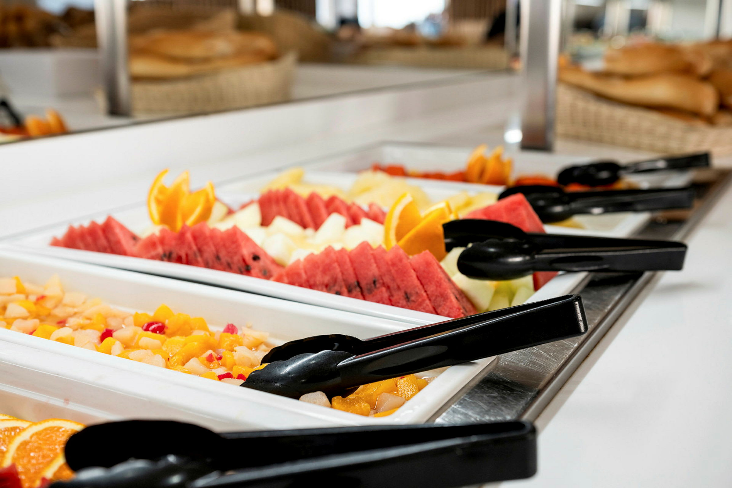 Buffet-pöytä, jossa tuoreita hedelmiä ja salaattia, mukaan lukien meloneja, appelsiiniviipaleita ja pihtejä. (Tekoälyn luoma teksti)
