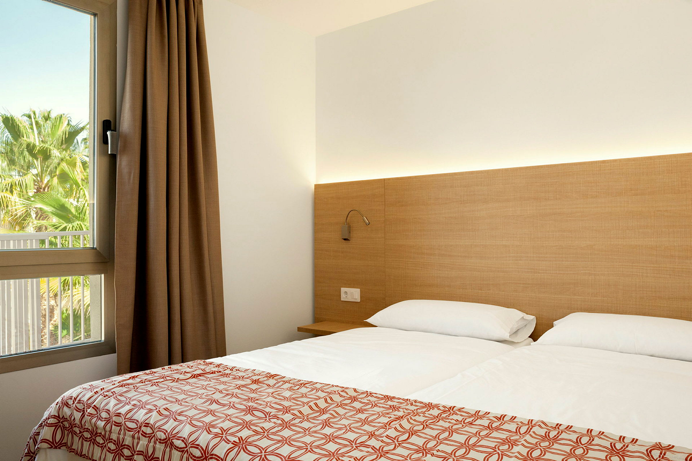 Moderni hotellihuone, jossa on parivuode, yöpöytä ja ikkuna näköalalla vehreyteen. (Tekoälyn luoma teksti)