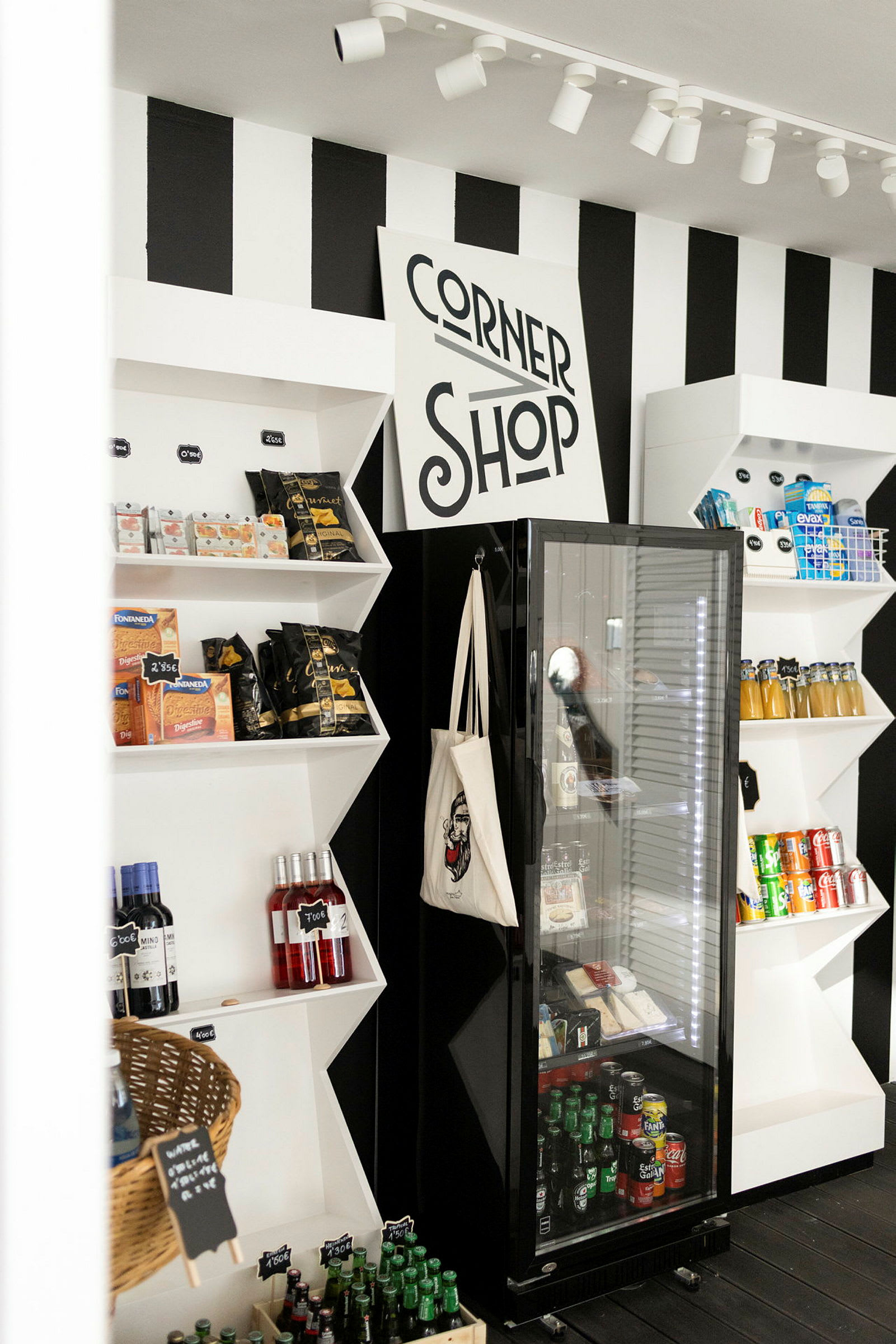 Pieni kauppa, jossa on kylttejä, joissa lukee 'Corner Shop'. Hyllyillä on erilaisia tuotteita, mukaan lukien välipaloja, juomia ja pulloja. (Tekoälyn luoma teksti)