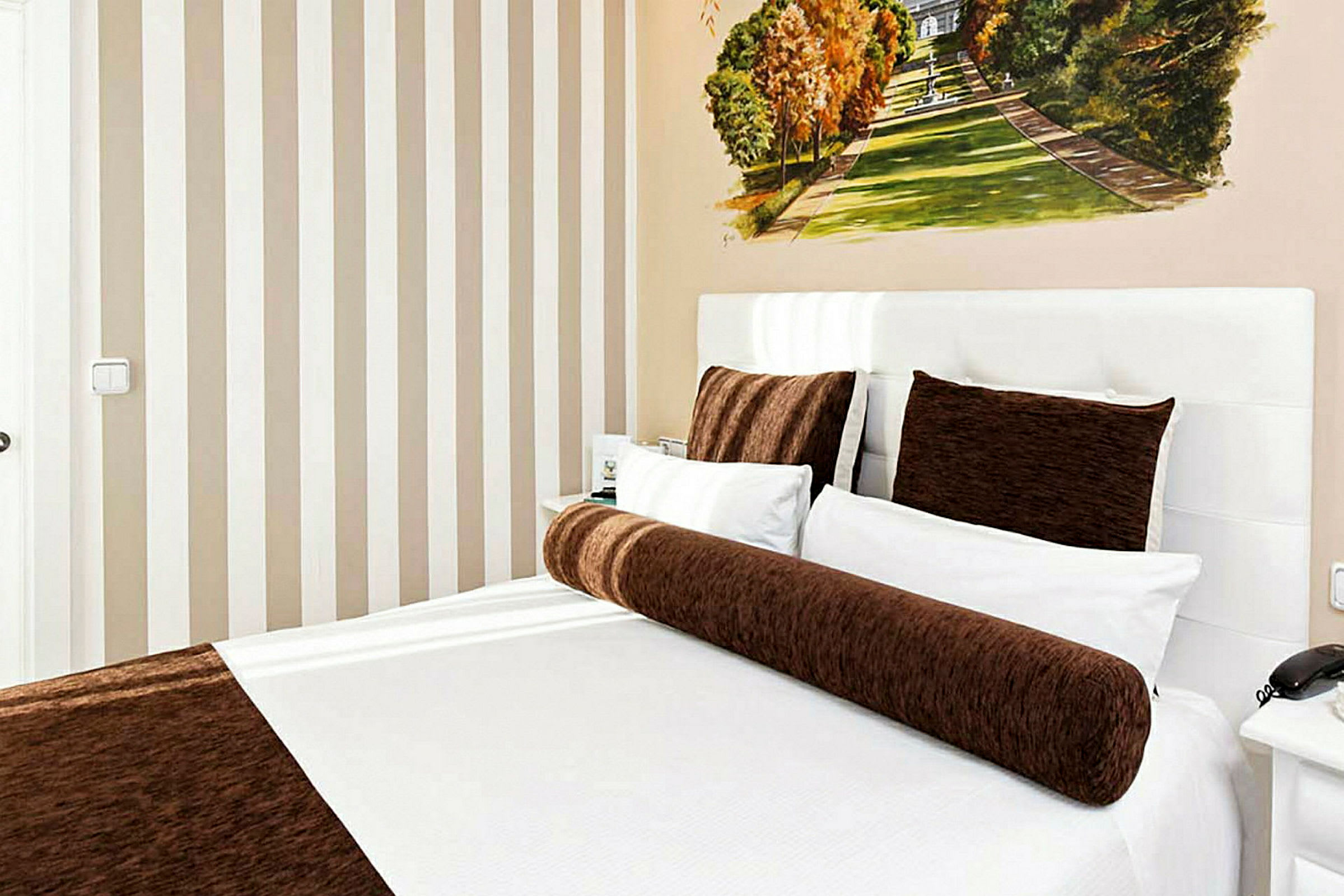 Hotellihuone, jossa sänky, jota on pedattu valkoisilla ja ruskeilla vuodevaatteilla. (Tekoälyn luoma teksti)
