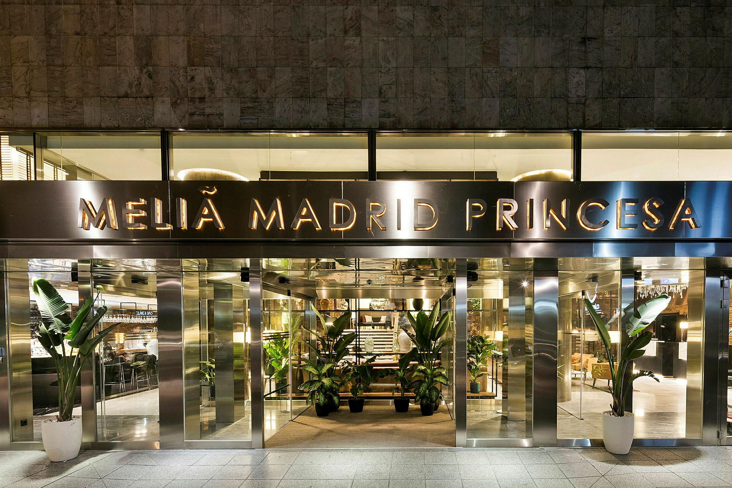 Hotelli Melia Madrid Princesan sisäänkäynti, jossa on lasiovet ja koristeelliset kasvit sisäänkäynnin luona. (Tekoälyn luoma teksti)
