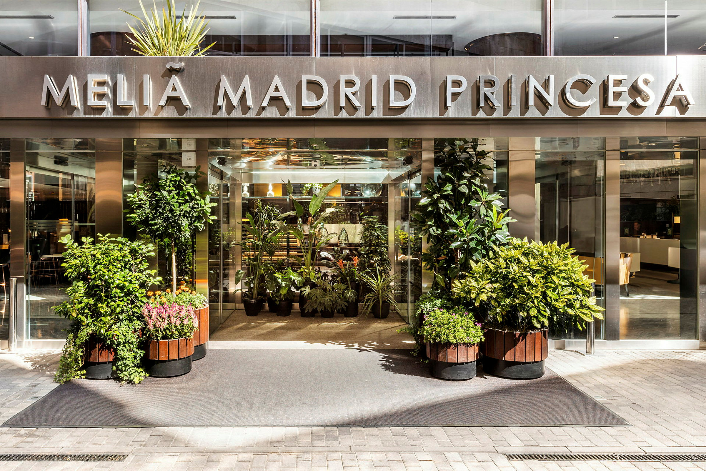 Hotellin sisäänkäynti, jossa kyltti "Meliá Madrid Princesa" ja ympärillä kasveja. (Tekoälyn luoma teksti)