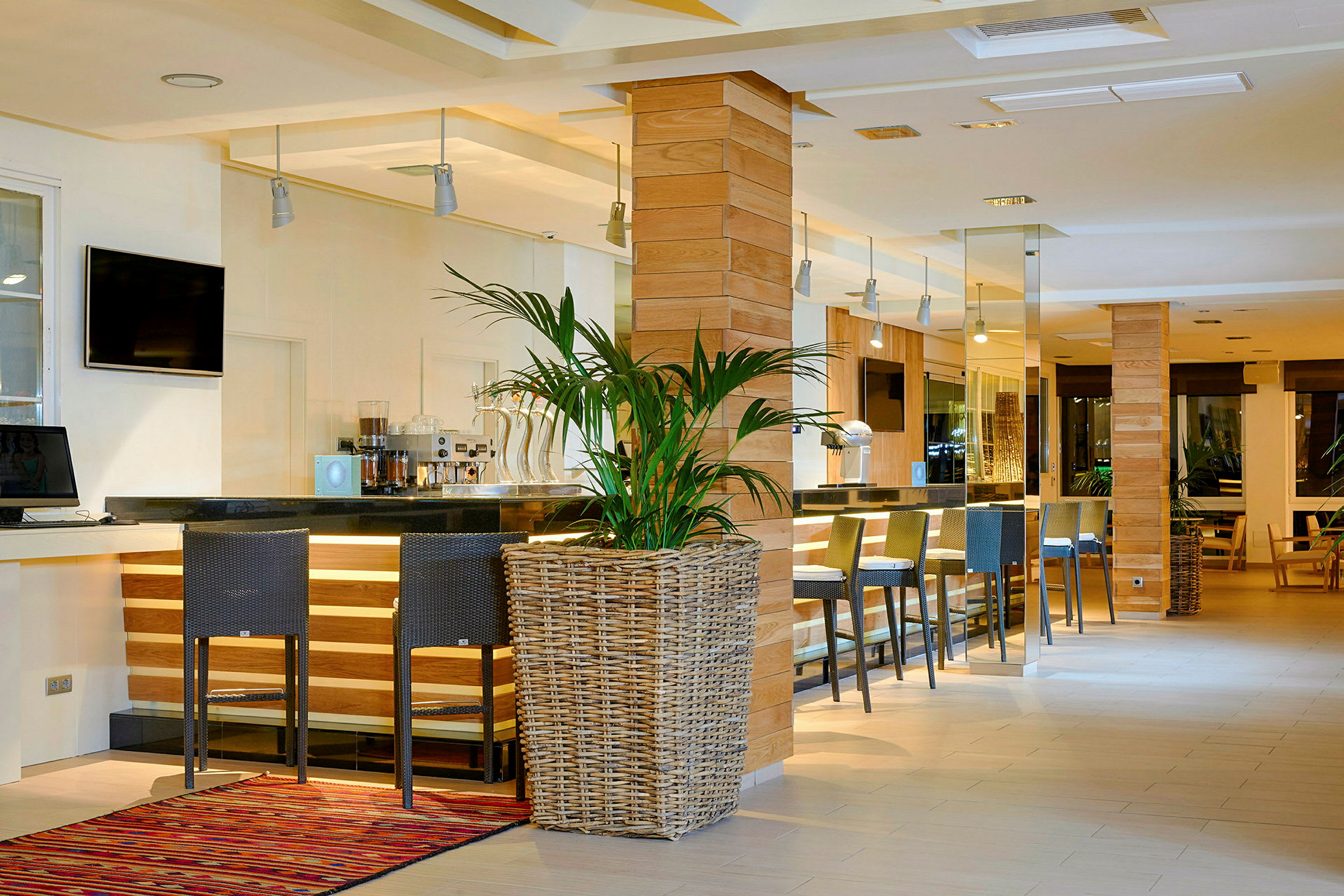 Kuva modernista ja tyylikkäästä hotellibaarista, jossa on korkeat tuolit, musta baaritiski, puupaneelit ja suuri ruukkukasvi etualalla. (Tekoälyn luoma teksti)