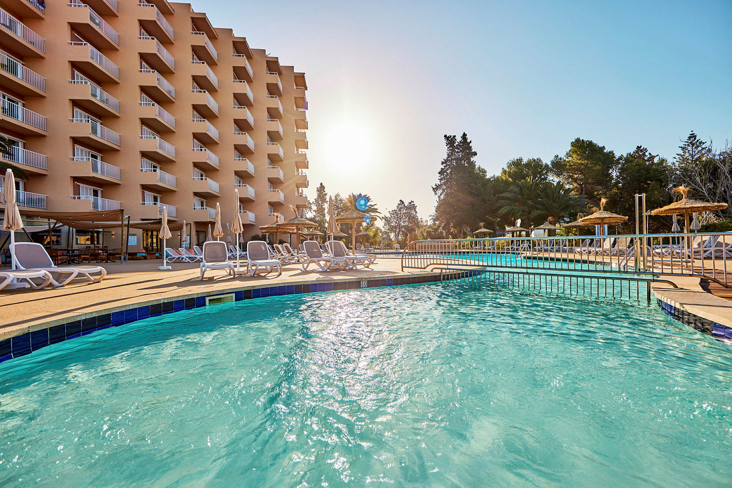 Kuva hotellista, jossa on parvekkeita, uima-allas ja aurinkotuoleja aurinkoisena päivänä. (Tekoälyn luoma teksti)